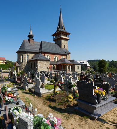 Zdjęcie nr 6: Kościół orientowany, trójnawowy, z niższym i węższym prezbiterium zakończonym absydą. Przy prezbiterium od strony południowej dostawiona kaplica na rzucie prostokąta, od północny analogiczna zakrystia, oba pomieszczenia nakryte dachami czterospadowymi. Do nawy od południa, na wysokości drugiego przęsła dostawiona zadaszona kruchta  wsparta na dwóch kamiennych filarach. Do elewacji zachodniej od południa i północy dostawione dwa aneksy na rzucie prostokąta nakryte dachami czterospadowymi. Nawa główna trójprzęsłowa, znacznie wyższa i szersza od naw bocznych, kryta stropem wspartym na murowanych z cegieł filarach o kompozytowych kapitelach. Doświetlona prostokątnymi oknami zamkniętymi łukiem półkolistym o podziale naśladującym triforium. Nawy boczne wydzielone od głównej półkolistymi arkadami, doświetlone okami w kształcie stojącego prostokąta zamkniętego półkoliście. Prezbiterium kryte prostym stropem oddzielone od nawy ścianą tęczową z półkolistą arkadą z profilowaną archiwoltą. Doświetlone wąskimi oknami w kształcie stojącego prostokąta zamkniętego łukiem półkolistym. Analogiczne okna w kaplicy południowej. W fasadzie czworoboczna zwężająca się ku górze wieża z drewnianą hurdycją, nakryta ostrosłupowym dachem zwieńczonym krzyżem. W przyziemiu portal nakryty wspartym na dwóch kamiennych filarach dachem półszczytowym. Powyżej prosty, drewniany krzyż oraz okrągła płycina mieszcząca tarczę zegarową. Elewacje licowane kamieniem, od południa i północy murowane z czerwonej cegły z kamiennymi obramieniami wokół okien. Dachy kryte blachą, ponad prezbiterium czworoboczna wieżyczka na sygnaturkę zwieńczona ostrosłupowym hełmem.