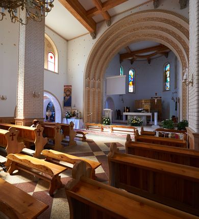 Zdjęcie nr 11: Kościół orientowany, trójnawowy, z niższym i węższym prezbiterium zakończonym absydą. Przy prezbiterium od strony południowej dostawiona kaplica na rzucie prostokąta, od północny analogiczna zakrystia, oba pomieszczenia nakryte dachami czterospadowymi. Do nawy od południa, na wysokości drugiego przęsła dostawiona zadaszona kruchta  wsparta na dwóch kamiennych filarach. Do elewacji zachodniej od południa i północy dostawione dwa aneksy na rzucie prostokąta nakryte dachami czterospadowymi. Nawa główna trójprzęsłowa, znacznie wyższa i szersza od naw bocznych, kryta stropem wspartym na murowanych z cegieł filarach o kompozytowych kapitelach. Doświetlona prostokątnymi oknami zamkniętymi łukiem półkolistym o podziale naśladującym triforium. Nawy boczne wydzielone od głównej półkolistymi arkadami, doświetlone okami w kształcie stojącego prostokąta zamkniętego półkoliście. Prezbiterium kryte prostym stropem oddzielone od nawy ścianą tęczową z półkolistą arkadą z profilowaną archiwoltą. Doświetlone wąskimi oknami w kształcie stojącego prostokąta zamkniętego łukiem półkolistym. Analogiczne okna w kaplicy południowej. W fasadzie czworoboczna zwężająca się ku górze wieża z drewnianą hurdycją, nakryta ostrosłupowym dachem zwieńczonym krzyżem. W przyziemiu portal nakryty wspartym na dwóch kamiennych filarach dachem półszczytowym. Powyżej prosty, drewniany krzyż oraz okrągła płycina mieszcząca tarczę zegarową. Elewacje licowane kamieniem, od południa i północy murowane z czerwonej cegły z kamiennymi obramieniami wokół okien. Dachy kryte blachą, ponad prezbiterium czworoboczna wieżyczka na sygnaturkę zwieńczona ostrosłupowym hełmem.