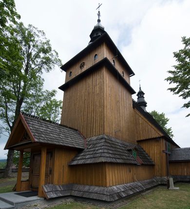 Zdjęcie nr 1: Kościół jest orientowany, drewniany, wzniesiony w konstrukcji zrębowej, o ścianach oszalowanych pionowo, z listwowaniem. Do korpusu nawowego, na rzucie zbliżonym do kwadratu, od wschodu przylega węższe, kwadratowe prezbiterium z dwukondygnacyjną zakrystią ze skarbcem od północy. Od zachodu do korpusu dobudowana jest wieża o konstrukcji słupowo-ramowej i pochyłych ścianach, z przedsionkiem w przyziemiu oraz z pozorną izbicą. Otoczona jest szalowanymi sobotami. Do wieży od zachodu i do korpusu od południa przylegają kruchty. Wnętrze przekryte jest stropami, w nawie z zaskrzynieniami. 
Korpus nawowy, prezbiterium i kruchty nakryte dachami dwuspadowymi, soboty pulpitowymi. Wszystkie dachy kryte gontem. Wieżę wieńczy baniasty hełm, kalenicę nad korpusem sygnaturka z latarnią. 
Ściany wnętrza zdobi figuralno-ornamentalna polichromia. Po zachodniej stronie korpusu nawowego usytuowany jest chór muzyczny wsparty na dwóch kolumnach.
Plac przykościelny otoczony jest murowanym ogrodzeniem oraz wieńcem starych lip.  
