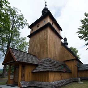 Zdjęcie nr 1: Kościół jest orientowany, drewniany, wzniesiony w konstrukcji zrębowej, o ścianach oszalowanych pionowo, z listwowaniem. Do korpusu nawowego, na rzucie zbliżonym do kwadratu, od wschodu przylega węższe, kwadratowe prezbiterium z dwukondygnacyjną zakrystią ze skarbcem od północy. Od zachodu do korpusu dobudowana jest wieża o konstrukcji słupowo-ramowej i pochyłych ścianach, z przedsionkiem w przyziemiu oraz z pozorną izbicą. Otoczona jest szalowanymi sobotami. Do wieży od zachodu i do korpusu od południa przylegają kruchty. Wnętrze przekryte jest stropami, w nawie z zaskrzynieniami. 
Korpus nawowy, prezbiterium i kruchty nakryte dachami dwuspadowymi, soboty pulpitowymi. Wszystkie dachy kryte gontem. Wieżę wieńczy baniasty hełm, kalenicę nad korpusem sygnaturka z latarnią. 
Ściany wnętrza zdobi figuralno-ornamentalna polichromia. Po zachodniej stronie korpusu nawowego usytuowany jest chór muzyczny wsparty na dwóch kolumnach.
Plac przykościelny otoczony jest murowanym ogrodzeniem oraz wieńcem starych lip.  
