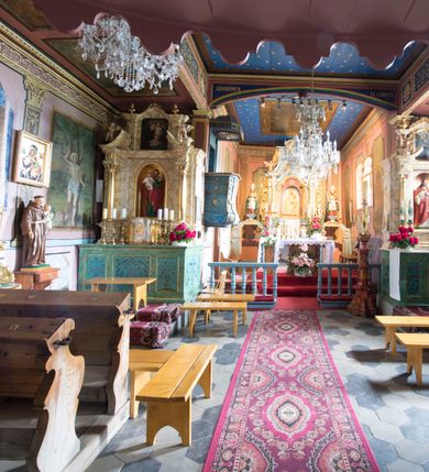 Zdjęcie nr 9: Kościół jest orientowany, drewniany, wzniesiony w konstrukcji zrębowej, o ścianach oszalowanych pionowo, z listwowaniem. Do korpusu nawowego, na rzucie zbliżonym do kwadratu, od wschodu przylega węższe, kwadratowe prezbiterium z dwukondygnacyjną zakrystią ze skarbcem od północy. Od zachodu do korpusu dobudowana jest wieża o konstrukcji słupowo-ramowej i pochyłych ścianach, z przedsionkiem w przyziemiu oraz z pozorną izbicą. Otoczona jest szalowanymi sobotami. Do wieży od zachodu i do korpusu od południa przylegają kruchty. Wnętrze przekryte jest stropami, w nawie z zaskrzynieniami. 
Korpus nawowy, prezbiterium i kruchty nakryte dachami dwuspadowymi, soboty pulpitowymi. Wszystkie dachy kryte gontem. Wieżę wieńczy baniasty hełm, kalenicę nad korpusem sygnaturka z latarnią. 
Ściany wnętrza zdobi figuralno-ornamentalna polichromia. Po zachodniej stronie korpusu nawowego usytuowany jest chór muzyczny wsparty na dwóch kolumnach.
Plac przykościelny otoczony jest murowanym ogrodzeniem oraz wieńcem starych lip.  
