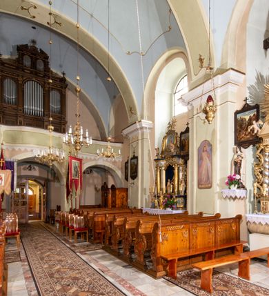 Zdjęcie nr 21: Kościół orientowany, murowany, tynkowany, jednonawowy, z prostokątną, trójprzęsłową nawą oraz węższym jednoprzęsłowym prezbiterium zamkniętym półkoliście, z dużą, prostokątną zakrystią przy północnej ścianie. Od zachodu wieża na planie kwadratu, do południowej ściany nawy dobudowana niewielka kruchta na planie kwadratu. 
Prezbiterium i nawa nakryte sklepieniem żagielkowym na gurtach spływających na pilastry. Otwór tęczowy w formie  arkady. W zachodniej części nawy parapet chóru muzycznego, o wklęsło-wypukłej balustradzie, wsparty na dwóch filarach i dwóch półfilarach, tworząc trzy arkady. Posadzka kamienna. 
Fasada wieżowa, z wejściem na osi w postaci drewnianego portyku nakrytego blaszanym daszkiem dwuspadowym. Wieża smukła, bez podziałów architektonicznych, zakończona dwoma profilowanymi gzymsami, wyłamującymi się na każdej ścianie na kształt łuku odcinkowego. Pomiędzy nimi, na ścianie frontowej tarcza zegarowa. W połowie wysokości wieży, z trzech stron niewielkie okna w formie stojącego prostokąta w okrągłych płycinach. W najwyższej partii ścian, z czterech stron, otwory dzwonne w formie stojącego prostokąta zamkniętego łukiem półkolistym. Wieża zwieńczona hełmem baniastym z latarnią, zakończoną kulą z krzyżem, pokrytym blachą. Elewacje bez podziałów, zakończone profilowanym gzymsem. W południowej cztery otwory okienne w formie stojącego prostokąta zamkniętego łukiem półkolistym, we wschodniej dwa analogiczne, w północnej jedno. 
Nawa i prezbiterium nakryte dachem dwuspadowym, blaszanym. W miejscu połączenia prezbiterium i nawy blaszana wieżyczka na sygnaturkę, z latarnią, zwieńczona hełmem baniastym z krzyżem. Zakrystia nakryta dachem trójspadowym, kruchta dachem falistym. Kościół otoczony niskim murem kamiennym.
