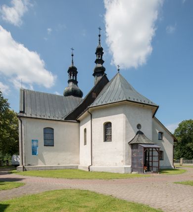 Zdjęcie nr 24: Kościół orientowany, murowany, jednonawowy, z prezbiterium, z zakrystią od północy i nawą z dwiema kaplicami – jedną od południa i drugą od północy. Od południa przylega do niego kruchta, a od zachodu wieża. Prezbiterium jest węższe od nawy, zamknięte wielobocznie, oddziela je tęcza o łuku półkolistym wsparta na pilastrach. Od zachodu chór na dwóch filarach, zamknięty balustradą wysuniętą przed lico w części środkowej i dekorowaną płycinami z umieszczonymi symetrycznie krzyżami łacińskimi. Ściany wnętrza gładkie, brak podziałów pionowych, partię ścian od sklepienia oddziela niebieski gzyms. Dół ścian wyłożony drewnianą boazerią, w prezbiterium kamiennymi płytami. Ściany przeprute oknami – prezbiterium czterema, nawa sześcioma w kształcie stojącego prostokąta zamkniętego łukiem odcinkowym, kolejne w kaplicach; większość wypełniają witraże. Główne wejście przez korpus wieżowy od zachodu, drugie od zakrystii. Elewacje kościoła są gładkie, narożniki podkreślone lizenami, wieża o dwóch kondygnacjach przedzielonych kapnikiem. W pierwszej wejście poniżej okna, od zachodu przypora, w drugiej cztery niewielkie okna. Dach jednokalenicowy, wieżyczka na sygnaturkę o kształcie barokowym, wieża przekryta hełmem baniastym z latarnią. Od zewnątrz, na wschodniej ścianie prezbiterium ogrójec w formie drewnianej altany. Do najstarszych elementów wyposażenia należą ołtarz główny z końca XVII wieku z wizerunkiem Matki Boskiej z Dzieciątkiem oraz osiemnastowieczne ołtarze boczne ustawione w nawie głównej. 