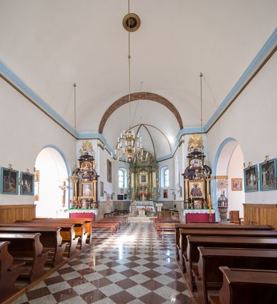 Zdjęcie nr 11: Kościół orientowany, murowany, jednonawowy, z prezbiterium, z zakrystią od północy i nawą z dwiema kaplicami – jedną od południa i drugą od północy. Od południa przylega do niego kruchta, a od zachodu wieża. Prezbiterium jest węższe od nawy, zamknięte wielobocznie, oddziela je tęcza o łuku półkolistym wsparta na pilastrach. Od zachodu chór na dwóch filarach, zamknięty balustradą wysuniętą przed lico w części środkowej i dekorowaną płycinami z umieszczonymi symetrycznie krzyżami łacińskimi. Ściany wnętrza gładkie, brak podziałów pionowych, partię ścian od sklepienia oddziela niebieski gzyms. Dół ścian wyłożony drewnianą boazerią, w prezbiterium kamiennymi płytami. Ściany przeprute oknami – prezbiterium czterema, nawa sześcioma w kształcie stojącego prostokąta zamkniętego łukiem odcinkowym, kolejne w kaplicach; większość wypełniają witraże. Główne wejście przez korpus wieżowy od zachodu, drugie od zakrystii. Elewacje kościoła są gładkie, narożniki podkreślone lizenami, wieża o dwóch kondygnacjach przedzielonych kapnikiem. W pierwszej wejście poniżej okna, od zachodu przypora, w drugiej cztery niewielkie okna. Dach jednokalenicowy, wieżyczka na sygnaturkę o kształcie barokowym, wieża przekryta hełmem baniastym z latarnią. Od zewnątrz, na wschodniej ścianie prezbiterium ogrójec w formie drewnianej altany. Do najstarszych elementów wyposażenia należą ołtarz główny z końca XVII wieku z wizerunkiem Matki Boskiej z Dzieciątkiem oraz osiemnastowieczne ołtarze boczne ustawione w nawie głównej. 
