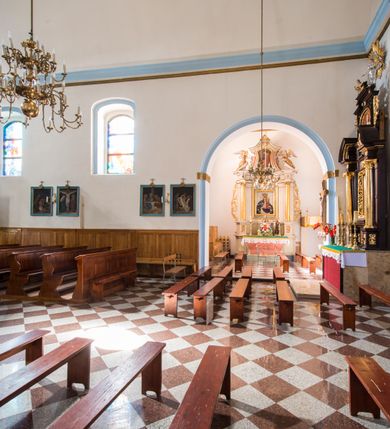 Zdjęcie nr 13: Kościół orientowany, murowany, jednonawowy, z prezbiterium, z zakrystią od północy i nawą z dwiema kaplicami – jedną od południa i drugą od północy. Od południa przylega do niego kruchta, a od zachodu wieża. Prezbiterium jest węższe od nawy, zamknięte wielobocznie, oddziela je tęcza o łuku półkolistym wsparta na pilastrach. Od zachodu chór na dwóch filarach, zamknięty balustradą wysuniętą przed lico w części środkowej i dekorowaną płycinami z umieszczonymi symetrycznie krzyżami łacińskimi. Ściany wnętrza gładkie, brak podziałów pionowych, partię ścian od sklepienia oddziela niebieski gzyms. Dół ścian wyłożony drewnianą boazerią, w prezbiterium kamiennymi płytami. Ściany przeprute oknami – prezbiterium czterema, nawa sześcioma w kształcie stojącego prostokąta zamkniętego łukiem odcinkowym, kolejne w kaplicach; większość wypełniają witraże. Główne wejście przez korpus wieżowy od zachodu, drugie od zakrystii. Elewacje kościoła są gładkie, narożniki podkreślone lizenami, wieża o dwóch kondygnacjach przedzielonych kapnikiem. W pierwszej wejście poniżej okna, od zachodu przypora, w drugiej cztery niewielkie okna. Dach jednokalenicowy, wieżyczka na sygnaturkę o kształcie barokowym, wieża przekryta hełmem baniastym z latarnią. Od zewnątrz, na wschodniej ścianie prezbiterium ogrójec w formie drewnianej altany. Do najstarszych elementów wyposażenia należą ołtarz główny z końca XVII wieku z wizerunkiem Matki Boskiej z Dzieciątkiem oraz osiemnastowieczne ołtarze boczne ustawione w nawie głównej. 