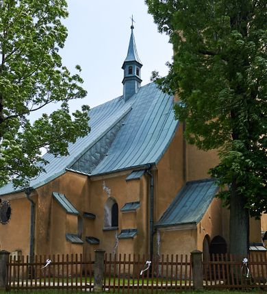Zdjęcie nr 13: Kościół murowany z cegły i kamienia, tynkowany. Zlokalizowany po północnej stronie wiejskiej drogi, na placu wydzielonym drewnianym płotem rozpiętym pomiędzy murowanymi, tynkowanymi filarami. Budowla orientowana, wzniesiona na wydłużonym rzucie złożonym z krótkiego, zamkniętego wielobocznie prezbiterium, nawy na rzucie zbliżonym  do kwadratu z centralnie umieszczonym filarem i wieży na rzucie kwadratu. Od północy do prezbiterium przylega zakrystia na rzucie kwadratu, do nawy kaplica na rzucie prostokąta. Do wieży dostawiony aneks z klatką schodową prowadzącą na chór. Od południa do nawy przylega kruchta na rzucie kwadratu. Całość budowli oszkarpowana w narożach. Wnętrze nakrywają sklepienia krzyżowe, w nawie żebra wsparte są na czworobocznym, murowanym filarze centralnym. W kruchcie pod wieżą sklepienie kryształowe, w zakrystii sieciowe. Otwory drzwiowe o wykroju ostrołukowym, w kamiennych portalach. Okna o wykroju stojących prostokątów, zwieńczonych łukiem pełnym; w północnej ścianie kaplicy okulus. Elewacje świątyni opracowane jednolicie, tynkowane, z niezbyt wydatnym gzymsem podokapowym, w narożach opięte masywnymi, trójuskokowymi przyporami. Elewacja zachodnia, wieżowa, czterokondygnacyjna, jednoosiowa, flankowana parą przypór. Gzyms kordonowy wydziela ostatnią, najwyższa kondygnację. W osi portal kamienny, zamknięty łukiem półkolistym. Powyżej, w osi okna w każdej z kondygnacji. Na pierwszym piętrze, w zworniku obramienia okiennego herb Drużyna w kartuszu. Boczne elewacje wieży bez otworów okiennych. Elewacja północna artykułowana przyporami, o nieregularnym układzie osi, przesłonięta przybudówkami kaplicy, zakrystii i klatki schodowej wiodącej na chór. W elewacji kaplicy, w osi okulus. W części prezbiterialnej okna o wykroju prostokąta zamkniętego łukiem półkolistym w dekoracyjnych obramieniach kamiennych z pilasterkami i archiwoltą zdobione płycinami i dekoracją ornamentalną w formie rozet i herbem Drużyna. Elewacja wschodnia artykułowana przyporami, przesłonięta parawanową ścianką drewnianą o trzech przeszklonych oknach-arkadah; w głębi ogrójec. Elewacja południowa artykułowana przyporami. W osi korpusu nawowego kruchta, ponad nią, po bokach dwa okna z obramieniami kamiennymi, dekorowanymi ornamentalnie i herbem Drużyna.  Dachy dwuspadowe, kryte blachą. Nieco wyższy nad korpusem nawowym, niższy nad prezbiterium. Nad zakrystią dach pulpitowy. Wieża zwieńczona cebulastym hełmem z latarnią.