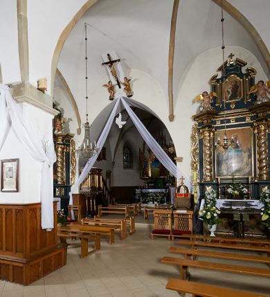 Zdjęcie nr 4: Kościół murowany z cegły i kamienia, tynkowany. Zlokalizowany po północnej stronie wiejskiej drogi, na placu wydzielonym drewnianym płotem rozpiętym pomiędzy murowanymi, tynkowanymi filarami. Budowla orientowana, wzniesiona na wydłużonym rzucie złożonym z krótkiego, zamkniętego wielobocznie prezbiterium, nawy na rzucie zbliżonym  do kwadratu z centralnie umieszczonym filarem i wieży na rzucie kwadratu. Od północy do prezbiterium przylega zakrystia na rzucie kwadratu, do nawy kaplica na rzucie prostokąta. Do wieży dostawiony aneks z klatką schodową prowadzącą na chór. Od południa do nawy przylega kruchta na rzucie kwadratu. Całość budowli oszkarpowana w narożach. Wnętrze nakrywają sklepienia krzyżowe, w nawie żebra wsparte są na czworobocznym, murowanym filarze centralnym. W kruchcie pod wieżą sklepienie kryształowe, w zakrystii sieciowe. Otwory drzwiowe o wykroju ostrołukowym, w kamiennych portalach. Okna o wykroju stojących prostokątów, zwieńczonych łukiem pełnym; w północnej ścianie kaplicy okulus. Elewacje świątyni opracowane jednolicie, tynkowane, z niezbyt wydatnym gzymsem podokapowym, w narożach opięte masywnymi, trójuskokowymi przyporami. Elewacja zachodnia, wieżowa, czterokondygnacyjna, jednoosiowa, flankowana parą przypór. Gzyms kordonowy wydziela ostatnią, najwyższa kondygnację. W osi portal kamienny, zamknięty łukiem półkolistym. Powyżej, w osi okna w każdej z kondygnacji. Na pierwszym piętrze, w zworniku obramienia okiennego herb Drużyna w kartuszu. Boczne elewacje wieży bez otworów okiennych. Elewacja północna artykułowana przyporami, o nieregularnym układzie osi, przesłonięta przybudówkami kaplicy, zakrystii i klatki schodowej wiodącej na chór. W elewacji kaplicy, w osi okulus. W części prezbiterialnej okna o wykroju prostokąta zamkniętego łukiem półkolistym w dekoracyjnych obramieniach kamiennych z pilasterkami i archiwoltą zdobione płycinami i dekoracją ornamentalną w formie rozet i herbem Drużyna. Elewacja wschodnia artykułowana przyporami, przesłonięta parawanową ścianką drewnianą o trzech przeszklonych oknach-arkadah; w głębi ogrójec. Elewacja południowa artykułowana przyporami. W osi korpusu nawowego kruchta, ponad nią, po bokach dwa okna z obramieniami kamiennymi, dekorowanymi ornamentalnie i herbem Drużyna.  Dachy dwuspadowe, kryte blachą. Nieco wyższy nad korpusem nawowym, niższy nad prezbiterium. Nad zakrystią dach pulpitowy. Wieża zwieńczona cebulastym hełmem z latarnią.