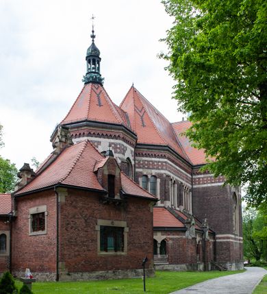 Zdjęcie nr 7: Kościół ceglany, jednonawowy z transeptem. Nawa artykułowana półfilarami i półkolumnami przechodzącymi w gurty sklepienia kolebkowego z lunetami w nawie głównej i żaglowego na przecięciu naw. Na ścianach polichromia na cegle, gurty podkreślone pasami wzorów geometrycznych, sklepienie niebieskie. W nawie i prezbiterium okna w formie biforiów, w transepcie w kształcie stojącego prostokąta zamkniętego łukiem pełnym, z maswerkami, w chórze węższe, zamknięte łukiem ostrym, dwudzielne z rozetą oraz biforia; główne wejście na osi. Chór muzyczny wsparty na masywnych filarach i kolumnach o kapitelach kostkowych z kamiennym parapetem ozdobionym fryzem arkadkowym. Na osi wieloplanowej fasady potężna, trójkondygnacyjna wieża. W pierwszej kondygnacji, po schodach wejście w formie łuku pełnego z drzwiami w formie stojącego prostokąta zamkniętego łukiem dwuramiennym. Obramienie wejścia kamienne, flankowane kolumnami z kostkowymi kapitelami, ze szczytem z chrystogramem. Całość wtopiona w szerszy szczyt, w zwieńczeniu którego rozeta. W trzeciej kondygnacji, zakomponowanej na drugim planie, okno w kształcie stojącego prostokąta zamkniętego łukiem pełnym, dwudzielne z rozetą. Nad nim rzeźba ukrzyżowanego Chrystusa, a w czterech narożach, na konsolach figury św. Stanisława biskupa, św. Stanisława Kostki, św. Jana Kantego i św. Kazimierza Jagiellończyka wykonane z kamienia pińczowskiego przez krakowskiego rzeźbiarza Władysława Druciaka. Wieżę flankują dwie mniejsze, również trójkondygnacyjne wieżyczki dołem czworoboczne, przechodzące w ośmiobok przepruty małymi, prostokątnymi oknami w dwóch niższych kondygnacjach i takimi samymi, naprzemiennie z biforiami w najwyższej. Elewacje transeptu z ogromnymi oknami dekorowanymi maswerkiem, zamknięte trójkątnymi szczytami. Elewacje zewnętrzne z wielobarwnej cegły – w większości ciemnej, dekorowanej na dwóch lub trzech poziomach pasami. Na poziomie pierwszej kondygnacji z jasnej cegły między pasami kamienia, poniżej linii dachu ze wzorem geometrycznym między pasami kamienia, w szczytach jasnym wzorem geometrycznym; chór dekorują blendy arkadkowe. Elewacje opinają ceglane szkarpy, w obejściu zwieńczone kamiennymi kapliczkami. Dachy nawy i transeptu dwuspadowe, dekorowane mozaiką geometryczną, wieloboczna kaplica z dachem sześciokątnym zwieńczonym barokową w kształcie wieżyczką na sygnaturkę, obejście pulpitowym. Do kaplicy przylega przełączka łącząca nowy kościół ze starym.  

Z wyposażenia kościoła na uwagę zasługują obraz Matki Boskiej Suskiej i dwie rzeźby (św. Łukasza i św. Jana Ewangelisty) przeniesione z ołtarza bocznego starego kościoła ustawione na ołtarzu głównym. Sam ołtarz główny (1912) wykonany został przez Antoniego Madeyskiego w Rzymie według rysunków Zygmunta Hendla. Madeyski wykorzystał do wzniesienia ołtarza rzadkie gatunki marmurów z rozebranego starochrześcijańskiego kościoła włoskiego. Niestety przerobiono go i zubożono w 1988 roku. Antoni Madeyski wykonał również tabernakulum, mensę ołtarzową, pulpit oraz chrzcielnicę. Teodor Talowski, architekt, zaprojektował również w 1901 roku ambonę z baldachimem. Zygmunt Hendel zaprojektował, prócz ołtarza głównego, ołtarz boczny św. Józefa i męki Pańskiej (1927). Franciszek Mączyński wykonał figurę Serca Pana Jezusa w latach 1914-1915. Za ołtarzem ze sceną Nawiedzenia widoczne są witraże według kartonów Zdzisława Giedliczki, w prezbiterium ze sceną Zesłania Ducha Świętego i postaciami Matki Boskiej Ostrobramskiej i św. Aleksandra.