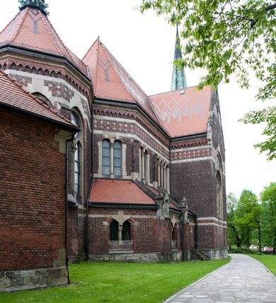 Zdjęcie nr 16: Kościół ceglany, jednonawowy z transeptem. Nawa artykułowana półfilarami i półkolumnami przechodzącymi w gurty sklepienia kolebkowego z lunetami w nawie głównej i żaglowego na przecięciu naw. Na ścianach polichromia na cegle, gurty podkreślone pasami wzorów geometrycznych, sklepienie niebieskie. W nawie i prezbiterium okna w formie biforiów, w transepcie w kształcie stojącego prostokąta zamkniętego łukiem pełnym, z maswerkami, w chórze węższe, zamknięte łukiem ostrym, dwudzielne z rozetą oraz biforia; główne wejście na osi. Chór muzyczny wsparty na masywnych filarach i kolumnach o kapitelach kostkowych z kamiennym parapetem ozdobionym fryzem arkadkowym. Na osi wieloplanowej fasady potężna, trójkondygnacyjna wieża. W pierwszej kondygnacji, po schodach wejście w formie łuku pełnego z drzwiami w formie stojącego prostokąta zamkniętego łukiem dwuramiennym. Obramienie wejścia kamienne, flankowane kolumnami z kostkowymi kapitelami, ze szczytem z chrystogramem. Całość wtopiona w szerszy szczyt, w zwieńczeniu którego rozeta. W trzeciej kondygnacji, zakomponowanej na drugim planie, okno w kształcie stojącego prostokąta zamkniętego łukiem pełnym, dwudzielne z rozetą. Nad nim rzeźba ukrzyżowanego Chrystusa, a w czterech narożach, na konsolach figury św. Stanisława biskupa, św. Stanisława Kostki, św. Jana Kantego i św. Kazimierza Jagiellończyka wykonane z kamienia pińczowskiego przez krakowskiego rzeźbiarza Władysława Druciaka. Wieżę flankują dwie mniejsze, również trójkondygnacyjne wieżyczki dołem czworoboczne, przechodzące w ośmiobok przepruty małymi, prostokątnymi oknami w dwóch niższych kondygnacjach i takimi samymi, naprzemiennie z biforiami w najwyższej. Elewacje transeptu z ogromnymi oknami dekorowanymi maswerkiem, zamknięte trójkątnymi szczytami. Elewacje zewnętrzne z wielobarwnej cegły – w większości ciemnej, dekorowanej na dwóch lub trzech poziomach pasami. Na poziomie pierwszej kondygnacji z jasnej cegły między pasami kamienia, poniżej linii dachu ze wzorem geometrycznym między pasami kamienia, w szczytach jasnym wzorem geometrycznym; chór dekorują blendy arkadkowe. Elewacje opinają ceglane szkarpy, w obejściu zwieńczone kamiennymi kapliczkami. Dachy nawy i transeptu dwuspadowe, dekorowane mozaiką geometryczną, wieloboczna kaplica z dachem sześciokątnym zwieńczonym barokową w kształcie wieżyczką na sygnaturkę, obejście pulpitowym. Do kaplicy przylega przełączka łącząca nowy kościół ze starym.  

Z wyposażenia kościoła na uwagę zasługują obraz Matki Boskiej Suskiej i dwie rzeźby (św. Łukasza i św. Jana Ewangelisty) przeniesione z ołtarza bocznego starego kościoła ustawione na ołtarzu głównym. Sam ołtarz główny (1912) wykonany został przez Antoniego Madeyskiego w Rzymie według rysunków Zygmunta Hendla. Madeyski wykorzystał do wzniesienia ołtarza rzadkie gatunki marmurów z rozebranego starochrześcijańskiego kościoła włoskiego. Niestety przerobiono go i zubożono w 1988 roku. Antoni Madeyski wykonał również tabernakulum, mensę ołtarzową, pulpit oraz chrzcielnicę. Teodor Talowski, architekt, zaprojektował również w 1901 roku ambonę z baldachimem. Zygmunt Hendel zaprojektował, prócz ołtarza głównego, ołtarz boczny św. Józefa i męki Pańskiej (1927). Franciszek Mączyński wykonał figurę Serca Pana Jezusa w latach 1914-1915. Za ołtarzem ze sceną Nawiedzenia widoczne są witraże według kartonów Zdzisława Giedliczki, w prezbiterium ze sceną Zesłania Ducha Świętego i postaciami Matki Boskiej Ostrobramskiej i św. Aleksandra.