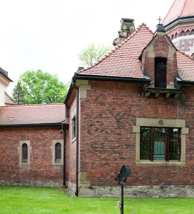 Zdjęcie nr 14: Kościół ceglany, jednonawowy z transeptem. Nawa artykułowana półfilarami i półkolumnami przechodzącymi w gurty sklepienia kolebkowego z lunetami w nawie głównej i żaglowego na przecięciu naw. Na ścianach polichromia na cegle, gurty podkreślone pasami wzorów geometrycznych, sklepienie niebieskie. W nawie i prezbiterium okna w formie biforiów, w transepcie w kształcie stojącego prostokąta zamkniętego łukiem pełnym, z maswerkami, w chórze węższe, zamknięte łukiem ostrym, dwudzielne z rozetą oraz biforia; główne wejście na osi. Chór muzyczny wsparty na masywnych filarach i kolumnach o kapitelach kostkowych z kamiennym parapetem ozdobionym fryzem arkadkowym. Na osi wieloplanowej fasady potężna, trójkondygnacyjna wieża. W pierwszej kondygnacji, po schodach wejście w formie łuku pełnego z drzwiami w formie stojącego prostokąta zamkniętego łukiem dwuramiennym. Obramienie wejścia kamienne, flankowane kolumnami z kostkowymi kapitelami, ze szczytem z chrystogramem. Całość wtopiona w szerszy szczyt, w zwieńczeniu którego rozeta. W trzeciej kondygnacji, zakomponowanej na drugim planie, okno w kształcie stojącego prostokąta zamkniętego łukiem pełnym, dwudzielne z rozetą. Nad nim rzeźba ukrzyżowanego Chrystusa, a w czterech narożach, na konsolach figury św. Stanisława biskupa, św. Stanisława Kostki, św. Jana Kantego i św. Kazimierza Jagiellończyka wykonane z kamienia pińczowskiego przez krakowskiego rzeźbiarza Władysława Druciaka. Wieżę flankują dwie mniejsze, również trójkondygnacyjne wieżyczki dołem czworoboczne, przechodzące w ośmiobok przepruty małymi, prostokątnymi oknami w dwóch niższych kondygnacjach i takimi samymi, naprzemiennie z biforiami w najwyższej. Elewacje transeptu z ogromnymi oknami dekorowanymi maswerkiem, zamknięte trójkątnymi szczytami. Elewacje zewnętrzne z wielobarwnej cegły – w większości ciemnej, dekorowanej na dwóch lub trzech poziomach pasami. Na poziomie pierwszej kondygnacji z jasnej cegły między pasami kamienia, poniżej linii dachu ze wzorem geometrycznym między pasami kamienia, w szczytach jasnym wzorem geometrycznym; chór dekorują blendy arkadkowe. Elewacje opinają ceglane szkarpy, w obejściu zwieńczone kamiennymi kapliczkami. Dachy nawy i transeptu dwuspadowe, dekorowane mozaiką geometryczną, wieloboczna kaplica z dachem sześciokątnym zwieńczonym barokową w kształcie wieżyczką na sygnaturkę, obejście pulpitowym. Do kaplicy przylega przełączka łącząca nowy kościół ze starym.  

Z wyposażenia kościoła na uwagę zasługują obraz Matki Boskiej Suskiej i dwie rzeźby (św. Łukasza i św. Jana Ewangelisty) przeniesione z ołtarza bocznego starego kościoła ustawione na ołtarzu głównym. Sam ołtarz główny (1912) wykonany został przez Antoniego Madeyskiego w Rzymie według rysunków Zygmunta Hendla. Madeyski wykorzystał do wzniesienia ołtarza rzadkie gatunki marmurów z rozebranego starochrześcijańskiego kościoła włoskiego. Niestety przerobiono go i zubożono w 1988 roku. Antoni Madeyski wykonał również tabernakulum, mensę ołtarzową, pulpit oraz chrzcielnicę. Teodor Talowski, architekt, zaprojektował również w 1901 roku ambonę z baldachimem. Zygmunt Hendel zaprojektował, prócz ołtarza głównego, ołtarz boczny św. Józefa i męki Pańskiej (1927). Franciszek Mączyński wykonał figurę Serca Pana Jezusa w latach 1914-1915. Za ołtarzem ze sceną Nawiedzenia widoczne są witraże według kartonów Zdzisława Giedliczki, w prezbiterium ze sceną Zesłania Ducha Świętego i postaciami Matki Boskiej Ostrobramskiej i św. Aleksandra.