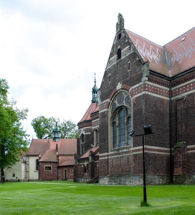 Zdjęcie nr 44: Kościół ceglany, jednonawowy z transeptem. Nawa artykułowana półfilarami i półkolumnami przechodzącymi w gurty sklepienia kolebkowego z lunetami w nawie głównej i żaglowego na przecięciu naw. Na ścianach polichromia na cegle, gurty podkreślone pasami wzorów geometrycznych, sklepienie niebieskie. W nawie i prezbiterium okna w formie biforiów, w transepcie w kształcie stojącego prostokąta zamkniętego łukiem pełnym, z maswerkami, w chórze węższe, zamknięte łukiem ostrym, dwudzielne z rozetą oraz biforia; główne wejście na osi. Chór muzyczny wsparty na masywnych filarach i kolumnach o kapitelach kostkowych z kamiennym parapetem ozdobionym fryzem arkadkowym. Na osi wieloplanowej fasady potężna, trójkondygnacyjna wieża. W pierwszej kondygnacji, po schodach wejście w formie łuku pełnego z drzwiami w formie stojącego prostokąta zamkniętego łukiem dwuramiennym. Obramienie wejścia kamienne, flankowane kolumnami z kostkowymi kapitelami, ze szczytem z chrystogramem. Całość wtopiona w szerszy szczyt, w zwieńczeniu którego rozeta. W trzeciej kondygnacji, zakomponowanej na drugim planie, okno w kształcie stojącego prostokąta zamkniętego łukiem pełnym, dwudzielne z rozetą. Nad nim rzeźba ukrzyżowanego Chrystusa, a w czterech narożach, na konsolach figury św. Stanisława biskupa, św. Stanisława Kostki, św. Jana Kantego i św. Kazimierza Jagiellończyka wykonane z kamienia pińczowskiego przez krakowskiego rzeźbiarza Władysława Druciaka. Wieżę flankują dwie mniejsze, również trójkondygnacyjne wieżyczki dołem czworoboczne, przechodzące w ośmiobok przepruty małymi, prostokątnymi oknami w dwóch niższych kondygnacjach i takimi samymi, naprzemiennie z biforiami w najwyższej. Elewacje transeptu z ogromnymi oknami dekorowanymi maswerkiem, zamknięte trójkątnymi szczytami. Elewacje zewnętrzne z wielobarwnej cegły – w większości ciemnej, dekorowanej na dwóch lub trzech poziomach pasami. Na poziomie pierwszej kondygnacji z jasnej cegły między pasami kamienia, poniżej linii dachu ze wzorem geometrycznym między pasami kamienia, w szczytach jasnym wzorem geometrycznym; chór dekorują blendy arkadkowe. Elewacje opinają ceglane szkarpy, w obejściu zwieńczone kamiennymi kapliczkami. Dachy nawy i transeptu dwuspadowe, dekorowane mozaiką geometryczną, wieloboczna kaplica z dachem sześciokątnym zwieńczonym barokową w kształcie wieżyczką na sygnaturkę, obejście pulpitowym. Do kaplicy przylega przełączka łącząca nowy kościół ze starym.  

Z wyposażenia kościoła na uwagę zasługują obraz Matki Boskiej Suskiej i dwie rzeźby (św. Łukasza i św. Jana Ewangelisty) przeniesione z ołtarza bocznego starego kościoła ustawione na ołtarzu głównym. Sam ołtarz główny (1912) wykonany został przez Antoniego Madeyskiego w Rzymie według rysunków Zygmunta Hendla. Madeyski wykorzystał do wzniesienia ołtarza rzadkie gatunki marmurów z rozebranego starochrześcijańskiego kościoła włoskiego. Niestety przerobiono go i zubożono w 1988 roku. Antoni Madeyski wykonał również tabernakulum, mensę ołtarzową, pulpit oraz chrzcielnicę. Teodor Talowski, architekt, zaprojektował również w 1901 roku ambonę z baldachimem. Zygmunt Hendel zaprojektował, prócz ołtarza głównego, ołtarz boczny św. Józefa i męki Pańskiej (1927). Franciszek Mączyński wykonał figurę Serca Pana Jezusa w latach 1914-1915. Za ołtarzem ze sceną Nawiedzenia widoczne są witraże według kartonów Zdzisława Giedliczki, w prezbiterium ze sceną Zesłania Ducha Świętego i postaciami Matki Boskiej Ostrobramskiej i św. Aleksandra.