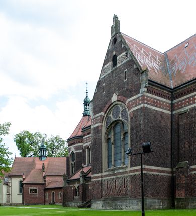 Zdjęcie nr 19: Kościół ceglany, jednonawowy z transeptem. Nawa artykułowana półfilarami i półkolumnami przechodzącymi w gurty sklepienia kolebkowego z lunetami w nawie głównej i żaglowego na przecięciu naw. Na ścianach polichromia na cegle, gurty podkreślone pasami wzorów geometrycznych, sklepienie niebieskie. W nawie i prezbiterium okna w formie biforiów, w transepcie w kształcie stojącego prostokąta zamkniętego łukiem pełnym, z maswerkami, w chórze węższe, zamknięte łukiem ostrym, dwudzielne z rozetą oraz biforia; główne wejście na osi. Chór muzyczny wsparty na masywnych filarach i kolumnach o kapitelach kostkowych z kamiennym parapetem ozdobionym fryzem arkadkowym. Na osi wieloplanowej fasady potężna, trójkondygnacyjna wieża. W pierwszej kondygnacji, po schodach wejście w formie łuku pełnego z drzwiami w formie stojącego prostokąta zamkniętego łukiem dwuramiennym. Obramienie wejścia kamienne, flankowane kolumnami z kostkowymi kapitelami, ze szczytem z chrystogramem. Całość wtopiona w szerszy szczyt, w zwieńczeniu którego rozeta. W trzeciej kondygnacji, zakomponowanej na drugim planie, okno w kształcie stojącego prostokąta zamkniętego łukiem pełnym, dwudzielne z rozetą. Nad nim rzeźba ukrzyżowanego Chrystusa, a w czterech narożach, na konsolach figury św. Stanisława biskupa, św. Stanisława Kostki, św. Jana Kantego i św. Kazimierza Jagiellończyka wykonane z kamienia pińczowskiego przez krakowskiego rzeźbiarza Władysława Druciaka. Wieżę flankują dwie mniejsze, również trójkondygnacyjne wieżyczki dołem czworoboczne, przechodzące w ośmiobok przepruty małymi, prostokątnymi oknami w dwóch niższych kondygnacjach i takimi samymi, naprzemiennie z biforiami w najwyższej. Elewacje transeptu z ogromnymi oknami dekorowanymi maswerkiem, zamknięte trójkątnymi szczytami. Elewacje zewnętrzne z wielobarwnej cegły – w większości ciemnej, dekorowanej na dwóch lub trzech poziomach pasami. Na poziomie pierwszej kondygnacji z jasnej cegły między pasami kamienia, poniżej linii dachu ze wzorem geometrycznym między pasami kamienia, w szczytach jasnym wzorem geometrycznym; chór dekorują blendy arkadkowe. Elewacje opinają ceglane szkarpy, w obejściu zwieńczone kamiennymi kapliczkami. Dachy nawy i transeptu dwuspadowe, dekorowane mozaiką geometryczną, wieloboczna kaplica z dachem sześciokątnym zwieńczonym barokową w kształcie wieżyczką na sygnaturkę, obejście pulpitowym. Do kaplicy przylega przełączka łącząca nowy kościół ze starym.  

Z wyposażenia kościoła na uwagę zasługują obraz Matki Boskiej Suskiej i dwie rzeźby (św. Łukasza i św. Jana Ewangelisty) przeniesione z ołtarza bocznego starego kościoła ustawione na ołtarzu głównym. Sam ołtarz główny (1912) wykonany został przez Antoniego Madeyskiego w Rzymie według rysunków Zygmunta Hendla. Madeyski wykorzystał do wzniesienia ołtarza rzadkie gatunki marmurów z rozebranego starochrześcijańskiego kościoła włoskiego. Niestety przerobiono go i zubożono w 1988 roku. Antoni Madeyski wykonał również tabernakulum, mensę ołtarzową, pulpit oraz chrzcielnicę. Teodor Talowski, architekt, zaprojektował również w 1901 roku ambonę z baldachimem. Zygmunt Hendel zaprojektował, prócz ołtarza głównego, ołtarz boczny św. Józefa i męki Pańskiej (1927). Franciszek Mączyński wykonał figurę Serca Pana Jezusa w latach 1914-1915. Za ołtarzem ze sceną Nawiedzenia widoczne są witraże według kartonów Zdzisława Giedliczki, w prezbiterium ze sceną Zesłania Ducha Świętego i postaciami Matki Boskiej Ostrobramskiej i św. Aleksandra.