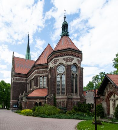 Zdjęcie nr 10: Kościół ceglany, jednonawowy z transeptem. Nawa artykułowana półfilarami i półkolumnami przechodzącymi w gurty sklepienia kolebkowego z lunetami w nawie głównej i żaglowego na przecięciu naw. Na ścianach polichromia na cegle, gurty podkreślone pasami wzorów geometrycznych, sklepienie niebieskie. W nawie i prezbiterium okna w formie biforiów, w transepcie w kształcie stojącego prostokąta zamkniętego łukiem pełnym, z maswerkami, w chórze węższe, zamknięte łukiem ostrym, dwudzielne z rozetą oraz biforia; główne wejście na osi. Chór muzyczny wsparty na masywnych filarach i kolumnach o kapitelach kostkowych z kamiennym parapetem ozdobionym fryzem arkadkowym. Na osi wieloplanowej fasady potężna, trójkondygnacyjna wieża. W pierwszej kondygnacji, po schodach wejście w formie łuku pełnego z drzwiami w formie stojącego prostokąta zamkniętego łukiem dwuramiennym. Obramienie wejścia kamienne, flankowane kolumnami z kostkowymi kapitelami, ze szczytem z chrystogramem. Całość wtopiona w szerszy szczyt, w zwieńczeniu którego rozeta. W trzeciej kondygnacji, zakomponowanej na drugim planie, okno w kształcie stojącego prostokąta zamkniętego łukiem pełnym, dwudzielne z rozetą. Nad nim rzeźba ukrzyżowanego Chrystusa, a w czterech narożach, na konsolach figury św. Stanisława biskupa, św. Stanisława Kostki, św. Jana Kantego i św. Kazimierza Jagiellończyka wykonane z kamienia pińczowskiego przez krakowskiego rzeźbiarza Władysława Druciaka. Wieżę flankują dwie mniejsze, również trójkondygnacyjne wieżyczki dołem czworoboczne, przechodzące w ośmiobok przepruty małymi, prostokątnymi oknami w dwóch niższych kondygnacjach i takimi samymi, naprzemiennie z biforiami w najwyższej. Elewacje transeptu z ogromnymi oknami dekorowanymi maswerkiem, zamknięte trójkątnymi szczytami. Elewacje zewnętrzne z wielobarwnej cegły – w większości ciemnej, dekorowanej na dwóch lub trzech poziomach pasami. Na poziomie pierwszej kondygnacji z jasnej cegły między pasami kamienia, poniżej linii dachu ze wzorem geometrycznym między pasami kamienia, w szczytach jasnym wzorem geometrycznym; chór dekorują blendy arkadkowe. Elewacje opinają ceglane szkarpy, w obejściu zwieńczone kamiennymi kapliczkami. Dachy nawy i transeptu dwuspadowe, dekorowane mozaiką geometryczną, wieloboczna kaplica z dachem sześciokątnym zwieńczonym barokową w kształcie wieżyczką na sygnaturkę, obejście pulpitowym. Do kaplicy przylega przełączka łącząca nowy kościół ze starym.  

Z wyposażenia kościoła na uwagę zasługują obraz Matki Boskiej Suskiej i dwie rzeźby (św. Łukasza i św. Jana Ewangelisty) przeniesione z ołtarza bocznego starego kościoła ustawione na ołtarzu głównym. Sam ołtarz główny (1912) wykonany został przez Antoniego Madeyskiego w Rzymie według rysunków Zygmunta Hendla. Madeyski wykorzystał do wzniesienia ołtarza rzadkie gatunki marmurów z rozebranego starochrześcijańskiego kościoła włoskiego. Niestety przerobiono go i zubożono w 1988 roku. Antoni Madeyski wykonał również tabernakulum, mensę ołtarzową, pulpit oraz chrzcielnicę. Teodor Talowski, architekt, zaprojektował również w 1901 roku ambonę z baldachimem. Zygmunt Hendel zaprojektował, prócz ołtarza głównego, ołtarz boczny św. Józefa i męki Pańskiej (1927). Franciszek Mączyński wykonał figurę Serca Pana Jezusa w latach 1914-1915. Za ołtarzem ze sceną Nawiedzenia widoczne są witraże według kartonów Zdzisława Giedliczki, w prezbiterium ze sceną Zesłania Ducha Świętego i postaciami Matki Boskiej Ostrobramskiej i św. Aleksandra.