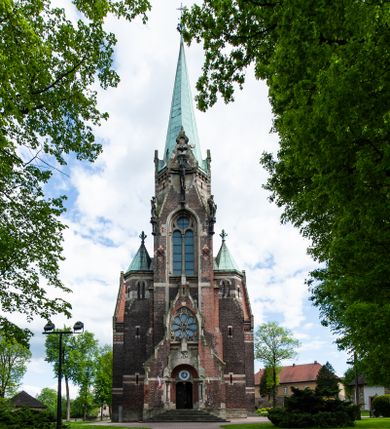 Zdjęcie nr 1: Kościół ceglany, jednonawowy z transeptem. Nawa artykułowana półfilarami i półkolumnami przechodzącymi w gurty sklepienia kolebkowego z lunetami w nawie głównej i żaglowego na przecięciu naw. Na ścianach polichromia na cegle, gurty podkreślone pasami wzorów geometrycznych, sklepienie niebieskie. W nawie i prezbiterium okna w formie biforiów, w transepcie w kształcie stojącego prostokąta zamkniętego łukiem pełnym, z maswerkami, w chórze węższe, zamknięte łukiem ostrym, dwudzielne z rozetą oraz biforia; główne wejście na osi. Chór muzyczny wsparty na masywnych filarach i kolumnach o kapitelach kostkowych z kamiennym parapetem ozdobionym fryzem arkadkowym. Na osi wieloplanowej fasady potężna, trójkondygnacyjna wieża. W pierwszej kondygnacji, po schodach wejście w formie łuku pełnego z drzwiami w formie stojącego prostokąta zamkniętego łukiem dwuramiennym. Obramienie wejścia kamienne, flankowane kolumnami z kostkowymi kapitelami, ze szczytem z chrystogramem. Całość wtopiona w szerszy szczyt, w zwieńczeniu którego rozeta. W trzeciej kondygnacji, zakomponowanej na drugim planie, okno w kształcie stojącego prostokąta zamkniętego łukiem pełnym, dwudzielne z rozetą. Nad nim rzeźba ukrzyżowanego Chrystusa, a w czterech narożach, na konsolach figury św. Stanisława biskupa, św. Stanisława Kostki, św. Jana Kantego i św. Kazimierza Jagiellończyka wykonane z kamienia pińczowskiego przez krakowskiego rzeźbiarza Władysława Druciaka. Wieżę flankują dwie mniejsze, również trójkondygnacyjne wieżyczki dołem czworoboczne, przechodzące w ośmiobok przepruty małymi, prostokątnymi oknami w dwóch niższych kondygnacjach i takimi samymi, naprzemiennie z biforiami w najwyższej. Elewacje transeptu z ogromnymi oknami dekorowanymi maswerkiem, zamknięte trójkątnymi szczytami. Elewacje zewnętrzne z wielobarwnej cegły – w większości ciemnej, dekorowanej na dwóch lub trzech poziomach pasami. Na poziomie pierwszej kondygnacji z jasnej cegły między pasami kamienia, poniżej linii dachu ze wzorem geometrycznym między pasami kamienia, w szczytach jasnym wzorem geometrycznym; chór dekorują blendy arkadkowe. Elewacje opinają ceglane szkarpy, w obejściu zwieńczone kamiennymi kapliczkami. Dachy nawy i transeptu dwuspadowe, dekorowane mozaiką geometryczną, wieloboczna kaplica z dachem sześciokątnym zwieńczonym barokową w kształcie wieżyczką na sygnaturkę, obejście pulpitowym. Do kaplicy przylega przełączka łącząca nowy kościół ze starym.  

Z wyposażenia kościoła na uwagę zasługują obraz Matki Boskiej Suskiej i dwie rzeźby (św. Łukasza i św. Jana Ewangelisty) przeniesione z ołtarza bocznego starego kościoła ustawione na ołtarzu głównym. Sam ołtarz główny (1912) wykonany został przez Antoniego Madeyskiego w Rzymie według rysunków Zygmunta Hendla. Madeyski wykorzystał do wzniesienia ołtarza rzadkie gatunki marmurów z rozebranego starochrześcijańskiego kościoła włoskiego. Niestety przerobiono go i zubożono w 1988 roku. Antoni Madeyski wykonał również tabernakulum, mensę ołtarzową, pulpit oraz chrzcielnicę. Teodor Talowski, architekt, zaprojektował również w 1901 roku ambonę z baldachimem. Zygmunt Hendel zaprojektował, prócz ołtarza głównego, ołtarz boczny św. Józefa i męki Pańskiej (1927). Franciszek Mączyński wykonał figurę Serca Pana Jezusa w latach 1914-1915. Za ołtarzem ze sceną Nawiedzenia widoczne są witraże według kartonów Zdzisława Giedliczki, w prezbiterium ze sceną Zesłania Ducha Świętego i postaciami Matki Boskiej Ostrobramskiej i św. Aleksandra.