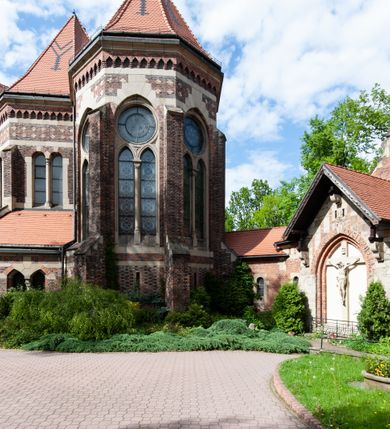 Zdjęcie nr 9: Kościół ceglany, jednonawowy z transeptem. Nawa artykułowana półfilarami i półkolumnami przechodzącymi w gurty sklepienia kolebkowego z lunetami w nawie głównej i żaglowego na przecięciu naw. Na ścianach polichromia na cegle, gurty podkreślone pasami wzorów geometrycznych, sklepienie niebieskie. W nawie i prezbiterium okna w formie biforiów, w transepcie w kształcie stojącego prostokąta zamkniętego łukiem pełnym, z maswerkami, w chórze węższe, zamknięte łukiem ostrym, dwudzielne z rozetą oraz biforia; główne wejście na osi. Chór muzyczny wsparty na masywnych filarach i kolumnach o kapitelach kostkowych z kamiennym parapetem ozdobionym fryzem arkadkowym. Na osi wieloplanowej fasady potężna, trójkondygnacyjna wieża. W pierwszej kondygnacji, po schodach wejście w formie łuku pełnego z drzwiami w formie stojącego prostokąta zamkniętego łukiem dwuramiennym. Obramienie wejścia kamienne, flankowane kolumnami z kostkowymi kapitelami, ze szczytem z chrystogramem. Całość wtopiona w szerszy szczyt, w zwieńczeniu którego rozeta. W trzeciej kondygnacji, zakomponowanej na drugim planie, okno w kształcie stojącego prostokąta zamkniętego łukiem pełnym, dwudzielne z rozetą. Nad nim rzeźba ukrzyżowanego Chrystusa, a w czterech narożach, na konsolach figury św. Stanisława biskupa, św. Stanisława Kostki, św. Jana Kantego i św. Kazimierza Jagiellończyka wykonane z kamienia pińczowskiego przez krakowskiego rzeźbiarza Władysława Druciaka. Wieżę flankują dwie mniejsze, również trójkondygnacyjne wieżyczki dołem czworoboczne, przechodzące w ośmiobok przepruty małymi, prostokątnymi oknami w dwóch niższych kondygnacjach i takimi samymi, naprzemiennie z biforiami w najwyższej. Elewacje transeptu z ogromnymi oknami dekorowanymi maswerkiem, zamknięte trójkątnymi szczytami. Elewacje zewnętrzne z wielobarwnej cegły – w większości ciemnej, dekorowanej na dwóch lub trzech poziomach pasami. Na poziomie pierwszej kondygnacji z jasnej cegły między pasami kamienia, poniżej linii dachu ze wzorem geometrycznym między pasami kamienia, w szczytach jasnym wzorem geometrycznym; chór dekorują blendy arkadkowe. Elewacje opinają ceglane szkarpy, w obejściu zwieńczone kamiennymi kapliczkami. Dachy nawy i transeptu dwuspadowe, dekorowane mozaiką geometryczną, wieloboczna kaplica z dachem sześciokątnym zwieńczonym barokową w kształcie wieżyczką na sygnaturkę, obejście pulpitowym. Do kaplicy przylega przełączka łącząca nowy kościół ze starym.  

Z wyposażenia kościoła na uwagę zasługują obraz Matki Boskiej Suskiej i dwie rzeźby (św. Łukasza i św. Jana Ewangelisty) przeniesione z ołtarza bocznego starego kościoła ustawione na ołtarzu głównym. Sam ołtarz główny (1912) wykonany został przez Antoniego Madeyskiego w Rzymie według rysunków Zygmunta Hendla. Madeyski wykorzystał do wzniesienia ołtarza rzadkie gatunki marmurów z rozebranego starochrześcijańskiego kościoła włoskiego. Niestety przerobiono go i zubożono w 1988 roku. Antoni Madeyski wykonał również tabernakulum, mensę ołtarzową, pulpit oraz chrzcielnicę. Teodor Talowski, architekt, zaprojektował również w 1901 roku ambonę z baldachimem. Zygmunt Hendel zaprojektował, prócz ołtarza głównego, ołtarz boczny św. Józefa i męki Pańskiej (1927). Franciszek Mączyński wykonał figurę Serca Pana Jezusa w latach 1914-1915. Za ołtarzem ze sceną Nawiedzenia widoczne są witraże według kartonów Zdzisława Giedliczki, w prezbiterium ze sceną Zesłania Ducha Świętego i postaciami Matki Boskiej Ostrobramskiej i św. Aleksandra.