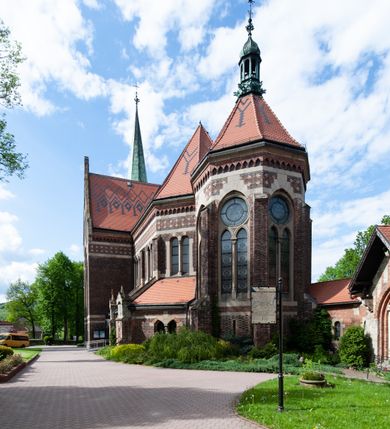 Zdjęcie nr 8: Kościół ceglany, jednonawowy z transeptem. Nawa artykułowana półfilarami i półkolumnami przechodzącymi w gurty sklepienia kolebkowego z lunetami w nawie głównej i żaglowego na przecięciu naw. Na ścianach polichromia na cegle, gurty podkreślone pasami wzorów geometrycznych, sklepienie niebieskie. W nawie i prezbiterium okna w formie biforiów, w transepcie w kształcie stojącego prostokąta zamkniętego łukiem pełnym, z maswerkami, w chórze węższe, zamknięte łukiem ostrym, dwudzielne z rozetą oraz biforia; główne wejście na osi. Chór muzyczny wsparty na masywnych filarach i kolumnach o kapitelach kostkowych z kamiennym parapetem ozdobionym fryzem arkadkowym. Na osi wieloplanowej fasady potężna, trójkondygnacyjna wieża. W pierwszej kondygnacji, po schodach wejście w formie łuku pełnego z drzwiami w formie stojącego prostokąta zamkniętego łukiem dwuramiennym. Obramienie wejścia kamienne, flankowane kolumnami z kostkowymi kapitelami, ze szczytem z chrystogramem. Całość wtopiona w szerszy szczyt, w zwieńczeniu którego rozeta. W trzeciej kondygnacji, zakomponowanej na drugim planie, okno w kształcie stojącego prostokąta zamkniętego łukiem pełnym, dwudzielne z rozetą. Nad nim rzeźba ukrzyżowanego Chrystusa, a w czterech narożach, na konsolach figury św. Stanisława biskupa, św. Stanisława Kostki, św. Jana Kantego i św. Kazimierza Jagiellończyka wykonane z kamienia pińczowskiego przez krakowskiego rzeźbiarza Władysława Druciaka. Wieżę flankują dwie mniejsze, również trójkondygnacyjne wieżyczki dołem czworoboczne, przechodzące w ośmiobok przepruty małymi, prostokątnymi oknami w dwóch niższych kondygnacjach i takimi samymi, naprzemiennie z biforiami w najwyższej. Elewacje transeptu z ogromnymi oknami dekorowanymi maswerkiem, zamknięte trójkątnymi szczytami. Elewacje zewnętrzne z wielobarwnej cegły – w większości ciemnej, dekorowanej na dwóch lub trzech poziomach pasami. Na poziomie pierwszej kondygnacji z jasnej cegły między pasami kamienia, poniżej linii dachu ze wzorem geometrycznym między pasami kamienia, w szczytach jasnym wzorem geometrycznym; chór dekorują blendy arkadkowe. Elewacje opinają ceglane szkarpy, w obejściu zwieńczone kamiennymi kapliczkami. Dachy nawy i transeptu dwuspadowe, dekorowane mozaiką geometryczną, wieloboczna kaplica z dachem sześciokątnym zwieńczonym barokową w kształcie wieżyczką na sygnaturkę, obejście pulpitowym. Do kaplicy przylega przełączka łącząca nowy kościół ze starym.  

Z wyposażenia kościoła na uwagę zasługują obraz Matki Boskiej Suskiej i dwie rzeźby (św. Łukasza i św. Jana Ewangelisty) przeniesione z ołtarza bocznego starego kościoła ustawione na ołtarzu głównym. Sam ołtarz główny (1912) wykonany został przez Antoniego Madeyskiego w Rzymie według rysunków Zygmunta Hendla. Madeyski wykorzystał do wzniesienia ołtarza rzadkie gatunki marmurów z rozebranego starochrześcijańskiego kościoła włoskiego. Niestety przerobiono go i zubożono w 1988 roku. Antoni Madeyski wykonał również tabernakulum, mensę ołtarzową, pulpit oraz chrzcielnicę. Teodor Talowski, architekt, zaprojektował również w 1901 roku ambonę z baldachimem. Zygmunt Hendel zaprojektował, prócz ołtarza głównego, ołtarz boczny św. Józefa i męki Pańskiej (1927). Franciszek Mączyński wykonał figurę Serca Pana Jezusa w latach 1914-1915. Za ołtarzem ze sceną Nawiedzenia widoczne są witraże według kartonów Zdzisława Giedliczki, w prezbiterium ze sceną Zesłania Ducha Świętego i postaciami Matki Boskiej Ostrobramskiej i św. Aleksandra.