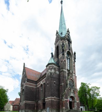 Zdjęcie nr 4: Kościół ceglany, jednonawowy z transeptem. Nawa artykułowana półfilarami i półkolumnami przechodzącymi w gurty sklepienia kolebkowego z lunetami w nawie głównej i żaglowego na przecięciu naw. Na ścianach polichromia na cegle, gurty podkreślone pasami wzorów geometrycznych, sklepienie niebieskie. W nawie i prezbiterium okna w formie biforiów, w transepcie w kształcie stojącego prostokąta zamkniętego łukiem pełnym, z maswerkami, w chórze węższe, zamknięte łukiem ostrym, dwudzielne z rozetą oraz biforia; główne wejście na osi. Chór muzyczny wsparty na masywnych filarach i kolumnach o kapitelach kostkowych z kamiennym parapetem ozdobionym fryzem arkadkowym. Na osi wieloplanowej fasady potężna, trójkondygnacyjna wieża. W pierwszej kondygnacji, po schodach wejście w formie łuku pełnego z drzwiami w formie stojącego prostokąta zamkniętego łukiem dwuramiennym. Obramienie wejścia kamienne, flankowane kolumnami z kostkowymi kapitelami, ze szczytem z chrystogramem. Całość wtopiona w szerszy szczyt, w zwieńczeniu którego rozeta. W trzeciej kondygnacji, zakomponowanej na drugim planie, okno w kształcie stojącego prostokąta zamkniętego łukiem pełnym, dwudzielne z rozetą. Nad nim rzeźba ukrzyżowanego Chrystusa, a w czterech narożach, na konsolach figury św. Stanisława biskupa, św. Stanisława Kostki, św. Jana Kantego i św. Kazimierza Jagiellończyka wykonane z kamienia pińczowskiego przez krakowskiego rzeźbiarza Władysława Druciaka. Wieżę flankują dwie mniejsze, również trójkondygnacyjne wieżyczki dołem czworoboczne, przechodzące w ośmiobok przepruty małymi, prostokątnymi oknami w dwóch niższych kondygnacjach i takimi samymi, naprzemiennie z biforiami w najwyższej. Elewacje transeptu z ogromnymi oknami dekorowanymi maswerkiem, zamknięte trójkątnymi szczytami. Elewacje zewnętrzne z wielobarwnej cegły – w większości ciemnej, dekorowanej na dwóch lub trzech poziomach pasami. Na poziomie pierwszej kondygnacji z jasnej cegły między pasami kamienia, poniżej linii dachu ze wzorem geometrycznym między pasami kamienia, w szczytach jasnym wzorem geometrycznym; chór dekorują blendy arkadkowe. Elewacje opinają ceglane szkarpy, w obejściu zwieńczone kamiennymi kapliczkami. Dachy nawy i transeptu dwuspadowe, dekorowane mozaiką geometryczną, wieloboczna kaplica z dachem sześciokątnym zwieńczonym barokową w kształcie wieżyczką na sygnaturkę, obejście pulpitowym. Do kaplicy przylega przełączka łącząca nowy kościół ze starym.  

Z wyposażenia kościoła na uwagę zasługują obraz Matki Boskiej Suskiej i dwie rzeźby (św. Łukasza i św. Jana Ewangelisty) przeniesione z ołtarza bocznego starego kościoła ustawione na ołtarzu głównym. Sam ołtarz główny (1912) wykonany został przez Antoniego Madeyskiego w Rzymie według rysunków Zygmunta Hendla. Madeyski wykorzystał do wzniesienia ołtarza rzadkie gatunki marmurów z rozebranego starochrześcijańskiego kościoła włoskiego. Niestety przerobiono go i zubożono w 1988 roku. Antoni Madeyski wykonał również tabernakulum, mensę ołtarzową, pulpit oraz chrzcielnicę. Teodor Talowski, architekt, zaprojektował również w 1901 roku ambonę z baldachimem. Zygmunt Hendel zaprojektował, prócz ołtarza głównego, ołtarz boczny św. Józefa i męki Pańskiej (1927). Franciszek Mączyński wykonał figurę Serca Pana Jezusa w latach 1914-1915. Za ołtarzem ze sceną Nawiedzenia widoczne są witraże według kartonów Zdzisława Giedliczki, w prezbiterium ze sceną Zesłania Ducha Świętego i postaciami Matki Boskiej Ostrobramskiej i św. Aleksandra.