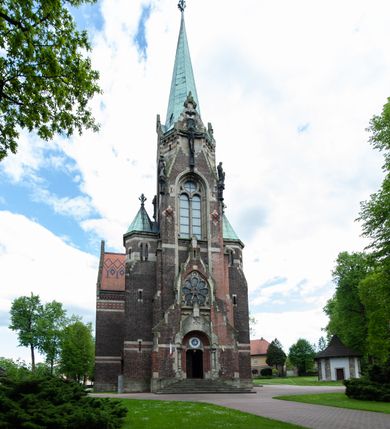 Zdjęcie nr 3: Kościół ceglany, jednonawowy z transeptem. Nawa artykułowana półfilarami i półkolumnami przechodzącymi w gurty sklepienia kolebkowego z lunetami w nawie głównej i żaglowego na przecięciu naw. Na ścianach polichromia na cegle, gurty podkreślone pasami wzorów geometrycznych, sklepienie niebieskie. W nawie i prezbiterium okna w formie biforiów, w transepcie w kształcie stojącego prostokąta zamkniętego łukiem pełnym, z maswerkami, w chórze węższe, zamknięte łukiem ostrym, dwudzielne z rozetą oraz biforia; główne wejście na osi. Chór muzyczny wsparty na masywnych filarach i kolumnach o kapitelach kostkowych z kamiennym parapetem ozdobionym fryzem arkadkowym. Na osi wieloplanowej fasady potężna, trójkondygnacyjna wieża. W pierwszej kondygnacji, po schodach wejście w formie łuku pełnego z drzwiami w formie stojącego prostokąta zamkniętego łukiem dwuramiennym. Obramienie wejścia kamienne, flankowane kolumnami z kostkowymi kapitelami, ze szczytem z chrystogramem. Całość wtopiona w szerszy szczyt, w zwieńczeniu którego rozeta. W trzeciej kondygnacji, zakomponowanej na drugim planie, okno w kształcie stojącego prostokąta zamkniętego łukiem pełnym, dwudzielne z rozetą. Nad nim rzeźba ukrzyżowanego Chrystusa, a w czterech narożach, na konsolach figury św. Stanisława biskupa, św. Stanisława Kostki, św. Jana Kantego i św. Kazimierza Jagiellończyka wykonane z kamienia pińczowskiego przez krakowskiego rzeźbiarza Władysława Druciaka. Wieżę flankują dwie mniejsze, również trójkondygnacyjne wieżyczki dołem czworoboczne, przechodzące w ośmiobok przepruty małymi, prostokątnymi oknami w dwóch niższych kondygnacjach i takimi samymi, naprzemiennie z biforiami w najwyższej. Elewacje transeptu z ogromnymi oknami dekorowanymi maswerkiem, zamknięte trójkątnymi szczytami. Elewacje zewnętrzne z wielobarwnej cegły – w większości ciemnej, dekorowanej na dwóch lub trzech poziomach pasami. Na poziomie pierwszej kondygnacji z jasnej cegły między pasami kamienia, poniżej linii dachu ze wzorem geometrycznym między pasami kamienia, w szczytach jasnym wzorem geometrycznym; chór dekorują blendy arkadkowe. Elewacje opinają ceglane szkarpy, w obejściu zwieńczone kamiennymi kapliczkami. Dachy nawy i transeptu dwuspadowe, dekorowane mozaiką geometryczną, wieloboczna kaplica z dachem sześciokątnym zwieńczonym barokową w kształcie wieżyczką na sygnaturkę, obejście pulpitowym. Do kaplicy przylega przełączka łącząca nowy kościół ze starym.  

Z wyposażenia kościoła na uwagę zasługują obraz Matki Boskiej Suskiej i dwie rzeźby (św. Łukasza i św. Jana Ewangelisty) przeniesione z ołtarza bocznego starego kościoła ustawione na ołtarzu głównym. Sam ołtarz główny (1912) wykonany został przez Antoniego Madeyskiego w Rzymie według rysunków Zygmunta Hendla. Madeyski wykorzystał do wzniesienia ołtarza rzadkie gatunki marmurów z rozebranego starochrześcijańskiego kościoła włoskiego. Niestety przerobiono go i zubożono w 1988 roku. Antoni Madeyski wykonał również tabernakulum, mensę ołtarzową, pulpit oraz chrzcielnicę. Teodor Talowski, architekt, zaprojektował również w 1901 roku ambonę z baldachimem. Zygmunt Hendel zaprojektował, prócz ołtarza głównego, ołtarz boczny św. Józefa i męki Pańskiej (1927). Franciszek Mączyński wykonał figurę Serca Pana Jezusa w latach 1914-1915. Za ołtarzem ze sceną Nawiedzenia widoczne są witraże według kartonów Zdzisława Giedliczki, w prezbiterium ze sceną Zesłania Ducha Świętego i postaciami Matki Boskiej Ostrobramskiej i św. Aleksandra.