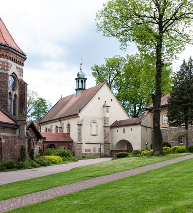 Zdjęcie nr 64: Kościół ceglany, jednonawowy z transeptem. Nawa artykułowana półfilarami i półkolumnami przechodzącymi w gurty sklepienia kolebkowego z lunetami w nawie głównej i żaglowego na przecięciu naw. Na ścianach polichromia na cegle, gurty podkreślone pasami wzorów geometrycznych, sklepienie niebieskie. W nawie i prezbiterium okna w formie biforiów, w transepcie w kształcie stojącego prostokąta zamkniętego łukiem pełnym, z maswerkami, w chórze węższe, zamknięte łukiem ostrym, dwudzielne z rozetą oraz biforia; główne wejście na osi. Chór muzyczny wsparty na masywnych filarach i kolumnach o kapitelach kostkowych z kamiennym parapetem ozdobionym fryzem arkadkowym. Na osi wieloplanowej fasady potężna, trójkondygnacyjna wieża. W pierwszej kondygnacji, po schodach wejście w formie łuku pełnego z drzwiami w formie stojącego prostokąta zamkniętego łukiem dwuramiennym. Obramienie wejścia kamienne, flankowane kolumnami z kostkowymi kapitelami, ze szczytem z chrystogramem. Całość wtopiona w szerszy szczyt, w zwieńczeniu którego rozeta. W trzeciej kondygnacji, zakomponowanej na drugim planie, okno w kształcie stojącego prostokąta zamkniętego łukiem pełnym, dwudzielne z rozetą. Nad nim rzeźba ukrzyżowanego Chrystusa, a w czterech narożach, na konsolach figury św. Stanisława biskupa, św. Stanisława Kostki, św. Jana Kantego i św. Kazimierza Jagiellończyka wykonane z kamienia pińczowskiego przez krakowskiego rzeźbiarza Władysława Druciaka. Wieżę flankują dwie mniejsze, również trójkondygnacyjne wieżyczki dołem czworoboczne, przechodzące w ośmiobok przepruty małymi, prostokątnymi oknami w dwóch niższych kondygnacjach i takimi samymi, naprzemiennie z biforiami w najwyższej. Elewacje transeptu z ogromnymi oknami dekorowanymi maswerkiem, zamknięte trójkątnymi szczytami. Elewacje zewnętrzne z wielobarwnej cegły – w większości ciemnej, dekorowanej na dwóch lub trzech poziomach pasami. Na poziomie pierwszej kondygnacji z jasnej cegły między pasami kamienia, poniżej linii dachu ze wzorem geometrycznym między pasami kamienia, w szczytach jasnym wzorem geometrycznym; chór dekorują blendy arkadkowe. Elewacje opinają ceglane szkarpy, w obejściu zwieńczone kamiennymi kapliczkami. Dachy nawy i transeptu dwuspadowe, dekorowane mozaiką geometryczną, wieloboczna kaplica z dachem sześciokątnym zwieńczonym barokową w kształcie wieżyczką na sygnaturkę, obejście pulpitowym. Do kaplicy przylega przełączka łącząca nowy kościół ze starym.  

Z wyposażenia kościoła na uwagę zasługują obraz Matki Boskiej Suskiej i dwie rzeźby (św. Łukasza i św. Jana Ewangelisty) przeniesione z ołtarza bocznego starego kościoła ustawione na ołtarzu głównym. Sam ołtarz główny (1912) wykonany został przez Antoniego Madeyskiego w Rzymie według rysunków Zygmunta Hendla. Madeyski wykorzystał do wzniesienia ołtarza rzadkie gatunki marmurów z rozebranego starochrześcijańskiego kościoła włoskiego. Niestety przerobiono go i zubożono w 1988 roku. Antoni Madeyski wykonał również tabernakulum, mensę ołtarzową, pulpit oraz chrzcielnicę. Teodor Talowski, architekt, zaprojektował również w 1901 roku ambonę z baldachimem. Zygmunt Hendel zaprojektował, prócz ołtarza głównego, ołtarz boczny św. Józefa i męki Pańskiej (1927). Franciszek Mączyński wykonał figurę Serca Pana Jezusa w latach 1914-1915. Za ołtarzem ze sceną Nawiedzenia widoczne są witraże według kartonów Zdzisława Giedliczki, w prezbiterium ze sceną Zesłania Ducha Świętego i postaciami Matki Boskiej Ostrobramskiej i św. Aleksandra.