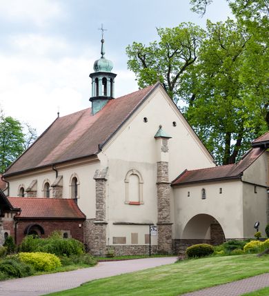 Zdjęcie nr 63: Kościół ceglany, jednonawowy z transeptem. Nawa artykułowana półfilarami i półkolumnami przechodzącymi w gurty sklepienia kolebkowego z lunetami w nawie głównej i żaglowego na przecięciu naw. Na ścianach polichromia na cegle, gurty podkreślone pasami wzorów geometrycznych, sklepienie niebieskie. W nawie i prezbiterium okna w formie biforiów, w transepcie w kształcie stojącego prostokąta zamkniętego łukiem pełnym, z maswerkami, w chórze węższe, zamknięte łukiem ostrym, dwudzielne z rozetą oraz biforia; główne wejście na osi. Chór muzyczny wsparty na masywnych filarach i kolumnach o kapitelach kostkowych z kamiennym parapetem ozdobionym fryzem arkadkowym. Na osi wieloplanowej fasady potężna, trójkondygnacyjna wieża. W pierwszej kondygnacji, po schodach wejście w formie łuku pełnego z drzwiami w formie stojącego prostokąta zamkniętego łukiem dwuramiennym. Obramienie wejścia kamienne, flankowane kolumnami z kostkowymi kapitelami, ze szczytem z chrystogramem. Całość wtopiona w szerszy szczyt, w zwieńczeniu którego rozeta. W trzeciej kondygnacji, zakomponowanej na drugim planie, okno w kształcie stojącego prostokąta zamkniętego łukiem pełnym, dwudzielne z rozetą. Nad nim rzeźba ukrzyżowanego Chrystusa, a w czterech narożach, na konsolach figury św. Stanisława biskupa, św. Stanisława Kostki, św. Jana Kantego i św. Kazimierza Jagiellończyka wykonane z kamienia pińczowskiego przez krakowskiego rzeźbiarza Władysława Druciaka. Wieżę flankują dwie mniejsze, również trójkondygnacyjne wieżyczki dołem czworoboczne, przechodzące w ośmiobok przepruty małymi, prostokątnymi oknami w dwóch niższych kondygnacjach i takimi samymi, naprzemiennie z biforiami w najwyższej. Elewacje transeptu z ogromnymi oknami dekorowanymi maswerkiem, zamknięte trójkątnymi szczytami. Elewacje zewnętrzne z wielobarwnej cegły – w większości ciemnej, dekorowanej na dwóch lub trzech poziomach pasami. Na poziomie pierwszej kondygnacji z jasnej cegły między pasami kamienia, poniżej linii dachu ze wzorem geometrycznym między pasami kamienia, w szczytach jasnym wzorem geometrycznym; chór dekorują blendy arkadkowe. Elewacje opinają ceglane szkarpy, w obejściu zwieńczone kamiennymi kapliczkami. Dachy nawy i transeptu dwuspadowe, dekorowane mozaiką geometryczną, wieloboczna kaplica z dachem sześciokątnym zwieńczonym barokową w kształcie wieżyczką na sygnaturkę, obejście pulpitowym. Do kaplicy przylega przełączka łącząca nowy kościół ze starym.  

Z wyposażenia kościoła na uwagę zasługują obraz Matki Boskiej Suskiej i dwie rzeźby (św. Łukasza i św. Jana Ewangelisty) przeniesione z ołtarza bocznego starego kościoła ustawione na ołtarzu głównym. Sam ołtarz główny (1912) wykonany został przez Antoniego Madeyskiego w Rzymie według rysunków Zygmunta Hendla. Madeyski wykorzystał do wzniesienia ołtarza rzadkie gatunki marmurów z rozebranego starochrześcijańskiego kościoła włoskiego. Niestety przerobiono go i zubożono w 1988 roku. Antoni Madeyski wykonał również tabernakulum, mensę ołtarzową, pulpit oraz chrzcielnicę. Teodor Talowski, architekt, zaprojektował również w 1901 roku ambonę z baldachimem. Zygmunt Hendel zaprojektował, prócz ołtarza głównego, ołtarz boczny św. Józefa i męki Pańskiej (1927). Franciszek Mączyński wykonał figurę Serca Pana Jezusa w latach 1914-1915. Za ołtarzem ze sceną Nawiedzenia widoczne są witraże według kartonów Zdzisława Giedliczki, w prezbiterium ze sceną Zesłania Ducha Świętego i postaciami Matki Boskiej Ostrobramskiej i św. Aleksandra.