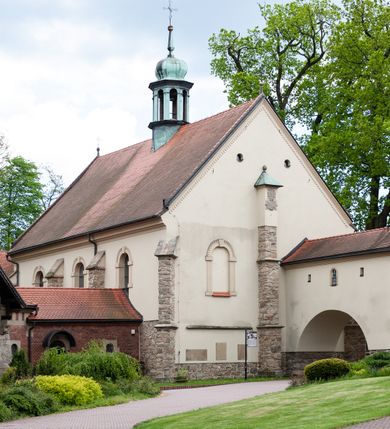 Zdjęcie nr 65: Kościół ceglany, jednonawowy z transeptem. Nawa artykułowana półfilarami i półkolumnami przechodzącymi w gurty sklepienia kolebkowego z lunetami w nawie głównej i żaglowego na przecięciu naw. Na ścianach polichromia na cegle, gurty podkreślone pasami wzorów geometrycznych, sklepienie niebieskie. W nawie i prezbiterium okna w formie biforiów, w transepcie w kształcie stojącego prostokąta zamkniętego łukiem pełnym, z maswerkami, w chórze węższe, zamknięte łukiem ostrym, dwudzielne z rozetą oraz biforia; główne wejście na osi. Chór muzyczny wsparty na masywnych filarach i kolumnach o kapitelach kostkowych z kamiennym parapetem ozdobionym fryzem arkadkowym. Na osi wieloplanowej fasady potężna, trójkondygnacyjna wieża. W pierwszej kondygnacji, po schodach wejście w formie łuku pełnego z drzwiami w formie stojącego prostokąta zamkniętego łukiem dwuramiennym. Obramienie wejścia kamienne, flankowane kolumnami z kostkowymi kapitelami, ze szczytem z chrystogramem. Całość wtopiona w szerszy szczyt, w zwieńczeniu którego rozeta. W trzeciej kondygnacji, zakomponowanej na drugim planie, okno w kształcie stojącego prostokąta zamkniętego łukiem pełnym, dwudzielne z rozetą. Nad nim rzeźba ukrzyżowanego Chrystusa, a w czterech narożach, na konsolach figury św. Stanisława biskupa, św. Stanisława Kostki, św. Jana Kantego i św. Kazimierza Jagiellończyka wykonane z kamienia pińczowskiego przez krakowskiego rzeźbiarza Władysława Druciaka. Wieżę flankują dwie mniejsze, również trójkondygnacyjne wieżyczki dołem czworoboczne, przechodzące w ośmiobok przepruty małymi, prostokątnymi oknami w dwóch niższych kondygnacjach i takimi samymi, naprzemiennie z biforiami w najwyższej. Elewacje transeptu z ogromnymi oknami dekorowanymi maswerkiem, zamknięte trójkątnymi szczytami. Elewacje zewnętrzne z wielobarwnej cegły – w większości ciemnej, dekorowanej na dwóch lub trzech poziomach pasami. Na poziomie pierwszej kondygnacji z jasnej cegły między pasami kamienia, poniżej linii dachu ze wzorem geometrycznym między pasami kamienia, w szczytach jasnym wzorem geometrycznym; chór dekorują blendy arkadkowe. Elewacje opinają ceglane szkarpy, w obejściu zwieńczone kamiennymi kapliczkami. Dachy nawy i transeptu dwuspadowe, dekorowane mozaiką geometryczną, wieloboczna kaplica z dachem sześciokątnym zwieńczonym barokową w kształcie wieżyczką na sygnaturkę, obejście pulpitowym. Do kaplicy przylega przełączka łącząca nowy kościół ze starym.  

Z wyposażenia kościoła na uwagę zasługują obraz Matki Boskiej Suskiej i dwie rzeźby (św. Łukasza i św. Jana Ewangelisty) przeniesione z ołtarza bocznego starego kościoła ustawione na ołtarzu głównym. Sam ołtarz główny (1912) wykonany został przez Antoniego Madeyskiego w Rzymie według rysunków Zygmunta Hendla. Madeyski wykorzystał do wzniesienia ołtarza rzadkie gatunki marmurów z rozebranego starochrześcijańskiego kościoła włoskiego. Niestety przerobiono go i zubożono w 1988 roku. Antoni Madeyski wykonał również tabernakulum, mensę ołtarzową, pulpit oraz chrzcielnicę. Teodor Talowski, architekt, zaprojektował również w 1901 roku ambonę z baldachimem. Zygmunt Hendel zaprojektował, prócz ołtarza głównego, ołtarz boczny św. Józefa i męki Pańskiej (1927). Franciszek Mączyński wykonał figurę Serca Pana Jezusa w latach 1914-1915. Za ołtarzem ze sceną Nawiedzenia widoczne są witraże według kartonów Zdzisława Giedliczki, w prezbiterium ze sceną Zesłania Ducha Świętego i postaciami Matki Boskiej Ostrobramskiej i św. Aleksandra.