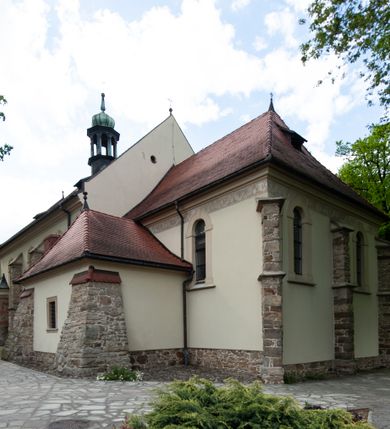 Zdjęcie nr 69: Kościół ceglany, jednonawowy z transeptem. Nawa artykułowana półfilarami i półkolumnami przechodzącymi w gurty sklepienia kolebkowego z lunetami w nawie głównej i żaglowego na przecięciu naw. Na ścianach polichromia na cegle, gurty podkreślone pasami wzorów geometrycznych, sklepienie niebieskie. W nawie i prezbiterium okna w formie biforiów, w transepcie w kształcie stojącego prostokąta zamkniętego łukiem pełnym, z maswerkami, w chórze węższe, zamknięte łukiem ostrym, dwudzielne z rozetą oraz biforia; główne wejście na osi. Chór muzyczny wsparty na masywnych filarach i kolumnach o kapitelach kostkowych z kamiennym parapetem ozdobionym fryzem arkadkowym. Na osi wieloplanowej fasady potężna, trójkondygnacyjna wieża. W pierwszej kondygnacji, po schodach wejście w formie łuku pełnego z drzwiami w formie stojącego prostokąta zamkniętego łukiem dwuramiennym. Obramienie wejścia kamienne, flankowane kolumnami z kostkowymi kapitelami, ze szczytem z chrystogramem. Całość wtopiona w szerszy szczyt, w zwieńczeniu którego rozeta. W trzeciej kondygnacji, zakomponowanej na drugim planie, okno w kształcie stojącego prostokąta zamkniętego łukiem pełnym, dwudzielne z rozetą. Nad nim rzeźba ukrzyżowanego Chrystusa, a w czterech narożach, na konsolach figury św. Stanisława biskupa, św. Stanisława Kostki, św. Jana Kantego i św. Kazimierza Jagiellończyka wykonane z kamienia pińczowskiego przez krakowskiego rzeźbiarza Władysława Druciaka. Wieżę flankują dwie mniejsze, również trójkondygnacyjne wieżyczki dołem czworoboczne, przechodzące w ośmiobok przepruty małymi, prostokątnymi oknami w dwóch niższych kondygnacjach i takimi samymi, naprzemiennie z biforiami w najwyższej. Elewacje transeptu z ogromnymi oknami dekorowanymi maswerkiem, zamknięte trójkątnymi szczytami. Elewacje zewnętrzne z wielobarwnej cegły – w większości ciemnej, dekorowanej na dwóch lub trzech poziomach pasami. Na poziomie pierwszej kondygnacji z jasnej cegły między pasami kamienia, poniżej linii dachu ze wzorem geometrycznym między pasami kamienia, w szczytach jasnym wzorem geometrycznym; chór dekorują blendy arkadkowe. Elewacje opinają ceglane szkarpy, w obejściu zwieńczone kamiennymi kapliczkami. Dachy nawy i transeptu dwuspadowe, dekorowane mozaiką geometryczną, wieloboczna kaplica z dachem sześciokątnym zwieńczonym barokową w kształcie wieżyczką na sygnaturkę, obejście pulpitowym. Do kaplicy przylega przełączka łącząca nowy kościół ze starym.  

Z wyposażenia kościoła na uwagę zasługują obraz Matki Boskiej Suskiej i dwie rzeźby (św. Łukasza i św. Jana Ewangelisty) przeniesione z ołtarza bocznego starego kościoła ustawione na ołtarzu głównym. Sam ołtarz główny (1912) wykonany został przez Antoniego Madeyskiego w Rzymie według rysunków Zygmunta Hendla. Madeyski wykorzystał do wzniesienia ołtarza rzadkie gatunki marmurów z rozebranego starochrześcijańskiego kościoła włoskiego. Niestety przerobiono go i zubożono w 1988 roku. Antoni Madeyski wykonał również tabernakulum, mensę ołtarzową, pulpit oraz chrzcielnicę. Teodor Talowski, architekt, zaprojektował również w 1901 roku ambonę z baldachimem. Zygmunt Hendel zaprojektował, prócz ołtarza głównego, ołtarz boczny św. Józefa i męki Pańskiej (1927). Franciszek Mączyński wykonał figurę Serca Pana Jezusa w latach 1914-1915. Za ołtarzem ze sceną Nawiedzenia widoczne są witraże według kartonów Zdzisława Giedliczki, w prezbiterium ze sceną Zesłania Ducha Świętego i postaciami Matki Boskiej Ostrobramskiej i św. Aleksandra.