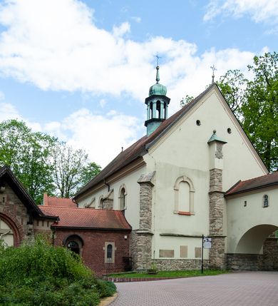 Zdjęcie nr 72: Kościół ceglany, jednonawowy z transeptem. Nawa artykułowana półfilarami i półkolumnami przechodzącymi w gurty sklepienia kolebkowego z lunetami w nawie głównej i żaglowego na przecięciu naw. Na ścianach polichromia na cegle, gurty podkreślone pasami wzorów geometrycznych, sklepienie niebieskie. W nawie i prezbiterium okna w formie biforiów, w transepcie w kształcie stojącego prostokąta zamkniętego łukiem pełnym, z maswerkami, w chórze węższe, zamknięte łukiem ostrym, dwudzielne z rozetą oraz biforia; główne wejście na osi. Chór muzyczny wsparty na masywnych filarach i kolumnach o kapitelach kostkowych z kamiennym parapetem ozdobionym fryzem arkadkowym. Na osi wieloplanowej fasady potężna, trójkondygnacyjna wieża. W pierwszej kondygnacji, po schodach wejście w formie łuku pełnego z drzwiami w formie stojącego prostokąta zamkniętego łukiem dwuramiennym. Obramienie wejścia kamienne, flankowane kolumnami z kostkowymi kapitelami, ze szczytem z chrystogramem. Całość wtopiona w szerszy szczyt, w zwieńczeniu którego rozeta. W trzeciej kondygnacji, zakomponowanej na drugim planie, okno w kształcie stojącego prostokąta zamkniętego łukiem pełnym, dwudzielne z rozetą. Nad nim rzeźba ukrzyżowanego Chrystusa, a w czterech narożach, na konsolach figury św. Stanisława biskupa, św. Stanisława Kostki, św. Jana Kantego i św. Kazimierza Jagiellończyka wykonane z kamienia pińczowskiego przez krakowskiego rzeźbiarza Władysława Druciaka. Wieżę flankują dwie mniejsze, również trójkondygnacyjne wieżyczki dołem czworoboczne, przechodzące w ośmiobok przepruty małymi, prostokątnymi oknami w dwóch niższych kondygnacjach i takimi samymi, naprzemiennie z biforiami w najwyższej. Elewacje transeptu z ogromnymi oknami dekorowanymi maswerkiem, zamknięte trójkątnymi szczytami. Elewacje zewnętrzne z wielobarwnej cegły – w większości ciemnej, dekorowanej na dwóch lub trzech poziomach pasami. Na poziomie pierwszej kondygnacji z jasnej cegły między pasami kamienia, poniżej linii dachu ze wzorem geometrycznym między pasami kamienia, w szczytach jasnym wzorem geometrycznym; chór dekorują blendy arkadkowe. Elewacje opinają ceglane szkarpy, w obejściu zwieńczone kamiennymi kapliczkami. Dachy nawy i transeptu dwuspadowe, dekorowane mozaiką geometryczną, wieloboczna kaplica z dachem sześciokątnym zwieńczonym barokową w kształcie wieżyczką na sygnaturkę, obejście pulpitowym. Do kaplicy przylega przełączka łącząca nowy kościół ze starym.  

Z wyposażenia kościoła na uwagę zasługują obraz Matki Boskiej Suskiej i dwie rzeźby (św. Łukasza i św. Jana Ewangelisty) przeniesione z ołtarza bocznego starego kościoła ustawione na ołtarzu głównym. Sam ołtarz główny (1912) wykonany został przez Antoniego Madeyskiego w Rzymie według rysunków Zygmunta Hendla. Madeyski wykorzystał do wzniesienia ołtarza rzadkie gatunki marmurów z rozebranego starochrześcijańskiego kościoła włoskiego. Niestety przerobiono go i zubożono w 1988 roku. Antoni Madeyski wykonał również tabernakulum, mensę ołtarzową, pulpit oraz chrzcielnicę. Teodor Talowski, architekt, zaprojektował również w 1901 roku ambonę z baldachimem. Zygmunt Hendel zaprojektował, prócz ołtarza głównego, ołtarz boczny św. Józefa i męki Pańskiej (1927). Franciszek Mączyński wykonał figurę Serca Pana Jezusa w latach 1914-1915. Za ołtarzem ze sceną Nawiedzenia widoczne są witraże według kartonów Zdzisława Giedliczki, w prezbiterium ze sceną Zesłania Ducha Świętego i postaciami Matki Boskiej Ostrobramskiej i św. Aleksandra.