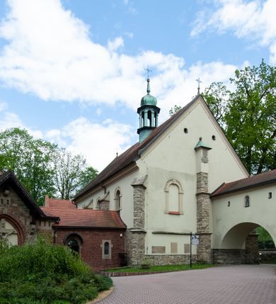 Zdjęcie nr 74: Kościół ceglany, jednonawowy z transeptem. Nawa artykułowana półfilarami i półkolumnami przechodzącymi w gurty sklepienia kolebkowego z lunetami w nawie głównej i żaglowego na przecięciu naw. Na ścianach polichromia na cegle, gurty podkreślone pasami wzorów geometrycznych, sklepienie niebieskie. W nawie i prezbiterium okna w formie biforiów, w transepcie w kształcie stojącego prostokąta zamkniętego łukiem pełnym, z maswerkami, w chórze węższe, zamknięte łukiem ostrym, dwudzielne z rozetą oraz biforia; główne wejście na osi. Chór muzyczny wsparty na masywnych filarach i kolumnach o kapitelach kostkowych z kamiennym parapetem ozdobionym fryzem arkadkowym. Na osi wieloplanowej fasady potężna, trójkondygnacyjna wieża. W pierwszej kondygnacji, po schodach wejście w formie łuku pełnego z drzwiami w formie stojącego prostokąta zamkniętego łukiem dwuramiennym. Obramienie wejścia kamienne, flankowane kolumnami z kostkowymi kapitelami, ze szczytem z chrystogramem. Całość wtopiona w szerszy szczyt, w zwieńczeniu którego rozeta. W trzeciej kondygnacji, zakomponowanej na drugim planie, okno w kształcie stojącego prostokąta zamkniętego łukiem pełnym, dwudzielne z rozetą. Nad nim rzeźba ukrzyżowanego Chrystusa, a w czterech narożach, na konsolach figury św. Stanisława biskupa, św. Stanisława Kostki, św. Jana Kantego i św. Kazimierza Jagiellończyka wykonane z kamienia pińczowskiego przez krakowskiego rzeźbiarza Władysława Druciaka. Wieżę flankują dwie mniejsze, również trójkondygnacyjne wieżyczki dołem czworoboczne, przechodzące w ośmiobok przepruty małymi, prostokątnymi oknami w dwóch niższych kondygnacjach i takimi samymi, naprzemiennie z biforiami w najwyższej. Elewacje transeptu z ogromnymi oknami dekorowanymi maswerkiem, zamknięte trójkątnymi szczytami. Elewacje zewnętrzne z wielobarwnej cegły – w większości ciemnej, dekorowanej na dwóch lub trzech poziomach pasami. Na poziomie pierwszej kondygnacji z jasnej cegły między pasami kamienia, poniżej linii dachu ze wzorem geometrycznym między pasami kamienia, w szczytach jasnym wzorem geometrycznym; chór dekorują blendy arkadkowe. Elewacje opinają ceglane szkarpy, w obejściu zwieńczone kamiennymi kapliczkami. Dachy nawy i transeptu dwuspadowe, dekorowane mozaiką geometryczną, wieloboczna kaplica z dachem sześciokątnym zwieńczonym barokową w kształcie wieżyczką na sygnaturkę, obejście pulpitowym. Do kaplicy przylega przełączka łącząca nowy kościół ze starym.  

Z wyposażenia kościoła na uwagę zasługują obraz Matki Boskiej Suskiej i dwie rzeźby (św. Łukasza i św. Jana Ewangelisty) przeniesione z ołtarza bocznego starego kościoła ustawione na ołtarzu głównym. Sam ołtarz główny (1912) wykonany został przez Antoniego Madeyskiego w Rzymie według rysunków Zygmunta Hendla. Madeyski wykorzystał do wzniesienia ołtarza rzadkie gatunki marmurów z rozebranego starochrześcijańskiego kościoła włoskiego. Niestety przerobiono go i zubożono w 1988 roku. Antoni Madeyski wykonał również tabernakulum, mensę ołtarzową, pulpit oraz chrzcielnicę. Teodor Talowski, architekt, zaprojektował również w 1901 roku ambonę z baldachimem. Zygmunt Hendel zaprojektował, prócz ołtarza głównego, ołtarz boczny św. Józefa i męki Pańskiej (1927). Franciszek Mączyński wykonał figurę Serca Pana Jezusa w latach 1914-1915. Za ołtarzem ze sceną Nawiedzenia widoczne są witraże według kartonów Zdzisława Giedliczki, w prezbiterium ze sceną Zesłania Ducha Świętego i postaciami Matki Boskiej Ostrobramskiej i św. Aleksandra.