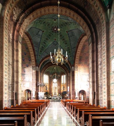 Zdjęcie nr 82: Kościół ceglany, jednonawowy z transeptem. Nawa artykułowana półfilarami i półkolumnami przechodzącymi w gurty sklepienia kolebkowego z lunetami w nawie głównej i żaglowego na przecięciu naw. Na ścianach polichromia na cegle, gurty podkreślone pasami wzorów geometrycznych, sklepienie niebieskie. W nawie i prezbiterium okna w formie biforiów, w transepcie w kształcie stojącego prostokąta zamkniętego łukiem pełnym, z maswerkami, w chórze węższe, zamknięte łukiem ostrym, dwudzielne z rozetą oraz biforia; główne wejście na osi. Chór muzyczny wsparty na masywnych filarach i kolumnach o kapitelach kostkowych z kamiennym parapetem ozdobionym fryzem arkadkowym. Na osi wieloplanowej fasady potężna, trójkondygnacyjna wieża. W pierwszej kondygnacji, po schodach wejście w formie łuku pełnego z drzwiami w formie stojącego prostokąta zamkniętego łukiem dwuramiennym. Obramienie wejścia kamienne, flankowane kolumnami z kostkowymi kapitelami, ze szczytem z chrystogramem. Całość wtopiona w szerszy szczyt, w zwieńczeniu którego rozeta. W trzeciej kondygnacji, zakomponowanej na drugim planie, okno w kształcie stojącego prostokąta zamkniętego łukiem pełnym, dwudzielne z rozetą. Nad nim rzeźba ukrzyżowanego Chrystusa, a w czterech narożach, na konsolach figury św. Stanisława biskupa, św. Stanisława Kostki, św. Jana Kantego i św. Kazimierza Jagiellończyka wykonane z kamienia pińczowskiego przez krakowskiego rzeźbiarza Władysława Druciaka. Wieżę flankują dwie mniejsze, również trójkondygnacyjne wieżyczki dołem czworoboczne, przechodzące w ośmiobok przepruty małymi, prostokątnymi oknami w dwóch niższych kondygnacjach i takimi samymi, naprzemiennie z biforiami w najwyższej. Elewacje transeptu z ogromnymi oknami dekorowanymi maswerkiem, zamknięte trójkątnymi szczytami. Elewacje zewnętrzne z wielobarwnej cegły – w większości ciemnej, dekorowanej na dwóch lub trzech poziomach pasami. Na poziomie pierwszej kondygnacji z jasnej cegły między pasami kamienia, poniżej linii dachu ze wzorem geometrycznym między pasami kamienia, w szczytach jasnym wzorem geometrycznym; chór dekorują blendy arkadkowe. Elewacje opinają ceglane szkarpy, w obejściu zwieńczone kamiennymi kapliczkami. Dachy nawy i transeptu dwuspadowe, dekorowane mozaiką geometryczną, wieloboczna kaplica z dachem sześciokątnym zwieńczonym barokową w kształcie wieżyczką na sygnaturkę, obejście pulpitowym. Do kaplicy przylega przełączka łącząca nowy kościół ze starym.  

Z wyposażenia kościoła na uwagę zasługują obraz Matki Boskiej Suskiej i dwie rzeźby (św. Łukasza i św. Jana Ewangelisty) przeniesione z ołtarza bocznego starego kościoła ustawione na ołtarzu głównym. Sam ołtarz główny (1912) wykonany został przez Antoniego Madeyskiego w Rzymie według rysunków Zygmunta Hendla. Madeyski wykorzystał do wzniesienia ołtarza rzadkie gatunki marmurów z rozebranego starochrześcijańskiego kościoła włoskiego. Niestety przerobiono go i zubożono w 1988 roku. Antoni Madeyski wykonał również tabernakulum, mensę ołtarzową, pulpit oraz chrzcielnicę. Teodor Talowski, architekt, zaprojektował również w 1901 roku ambonę z baldachimem. Zygmunt Hendel zaprojektował, prócz ołtarza głównego, ołtarz boczny św. Józefa i męki Pańskiej (1927). Franciszek Mączyński wykonał figurę Serca Pana Jezusa w latach 1914-1915. Za ołtarzem ze sceną Nawiedzenia widoczne są witraże według kartonów Zdzisława Giedliczki, w prezbiterium ze sceną Zesłania Ducha Świętego i postaciami Matki Boskiej Ostrobramskiej i św. Aleksandra.