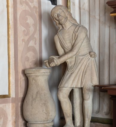 Zdjęcie nr 1: Na szerokim, ćwierćkolistym, wybrzuszonym cokole wmurowanym w północno-wschodni narożnik kaplicy ustawiona kamienna, całopostaciowa, pełnoplastyczna figura Chrystusa. Jezus stojąc zwrócony w trzech czwartych w prawo jest pochylony do przodu, z rękami skrępowanymi sznurem. Lekko przechyloną w prawo głowę charakteryzuje pociągła twarz o sumarycznie opracowanych rysach, małych oczach, prostym nosie i z krótkim zarostem. Długie, falowane włosy opadają na plecy. Nagą sylwetkę sumarycznie modelowaną w partii bioder przesłania sięgające kolan, lekko fałdowane perizonium związane na lewym boku. Krępujący  dłonie sznur w formie szerokiej pętli jest narzucony na ramiona Jezusa. 
Kolumna w kształcie pojedynczej tralki umieszczonej na czworobocznej podstawie. 
 Na cokole napis ujęty prostokątną ramką o wklęsłych narożach „PATRZ GRZESNIKU CO CIERPIĘ I NA MOIE RANY / NIE BICZUY MIE GRZECHAMI BOM DOSC SKA/TOWANY FONDATOR JAN HOŁUJ 1852”.
