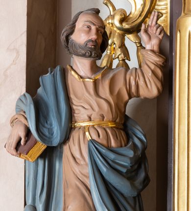 Zdjęcie nr 1: Całopostaciowa, drążona z tyłu figura św. Piotra stojącego w wydatnym kontrapoście na niewysokiej postawie i zwróconego w trzech czwartych w lewo. Twarz owalna o wysokim czole z zakolami, skierowanym lekko ku górze wzroku, uniesionych brwiach, z długim prostym nosem i krótkim, brązowym zarostem. Lekko falowane, krótkie włosy opadają na kark. Święty ubrany w beżową, sięgającą do połowy łydek suknię z długimi rękawami, przewiązaną złotym paskiem oraz niebieski płaszcz zarzucony na prawe ramię i opadający na plecy i podpięty do paska sukni. Na stopach złocone sandały. Święty prawą ręką podtrzymuje czerwoną księgę, lewą, zgiętą w łokciu unosi do góry z wyprostowanymi dwoma palcami. Draperia sukni delikatna, płaszcza o głębokich, dużych fałdach.