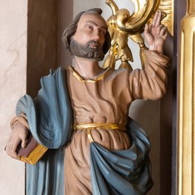 Zdjęcie nr 1: Całopostaciowa, drążona z tyłu figura św. Piotra stojącego w wydatnym kontrapoście na niewysokiej postawie i zwróconego w trzech czwartych w lewo. Twarz owalna o wysokim czole z zakolami, skierowanym lekko ku górze wzroku, uniesionych brwiach, z długim prostym nosem i krótkim, brązowym zarostem. Lekko falowane, krótkie włosy opadają na kark. Święty ubrany w beżową, sięgającą do połowy łydek suknię z długimi rękawami, przewiązaną złotym paskiem oraz niebieski płaszcz zarzucony na prawe ramię i opadający na plecy i podpięty do paska sukni. Na stopach złocone sandały. Święty prawą ręką podtrzymuje czerwoną księgę, lewą, zgiętą w łokciu unosi do góry z wyprostowanymi dwoma palcami. Draperia sukni delikatna, płaszcza o głębokich, dużych fałdach.