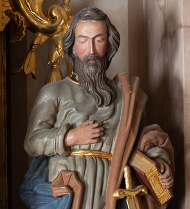Zdjęcie nr 1: Całopostaciowa, drążona z tyłu figura św. Pawła stojącego w kontrapoście na niewysokiej postawie i zwróconego na wprost. Lekko pochyloną głowę charakteryzuje pociągła twarz o półprzymkniętych oczach, długim prostym nosie i długim, brązowym zaroście. Lekko falowane włosy opadają na kark. Święty ubrany jest w oliwkowozieloną, sięgającą do połowy łydek suknię z długimi rękawami, przewiązaną złotym paskiem oraz niebieski płaszcz o brązowym podszyciu, zarzucony na lewę ramię i opadający na plecy, osłaniając prawe biodro. Buty jasnobrązowe, z wysoką cholewą o złotym brzegu. U pasa zatknięty długi, złocony miecz. Święty prawą dłoń wspiera na piersiach, w lewej trzyma zamkniętą księgę. Draperia sukni delikatna, płaszcza o głębokich, dużych fałdach.
