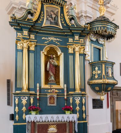 Zdjęcie nr 2: Ołtarz architektoniczny, jednokondygnacyjny, jednoosiowy, ze zwieńczeniem. Ołtarz prostopadłościenny, z drewnianą mensą i kamiennym portatylem. Antenpedium z płyciną w kształcie leżącego prostokąta, ujętą profilowaną, srebrzona ramą, z płaskorzeźbionym, złoconym i srebrzonym przedstawieniem Baranka Paschalnego na tle tarczy słonecznej. Retabulum na wysokim, zdwojonym cokole, o zryzalitowanych, uskokowych bokach, ujęte dwoma parami pilastrów i parą kolumn o kapitelach korynckich i żłobkowanych trzonach, podtrzymujących wyłamujące się ponad nimi, przerwane w partii architrawu i fryzu belkowanie z silnie wysuniętym gzymsem. Zwieńczenie ujęte parą spływów, zamknięte gzymsem w formie nadwieszonego łuku wycinkowego, flankowane fragmentami przerwanego przyczółka. Szczyt w formie promienistej glorii z motywem krzyża pośrodku. Górny cokół retabulum zdobiony motywem przewiązanych wstęgą kampanulli, pośrodku konsolka z polem w kształcie stojącego prostokąta zamkniętego półkoliście z monogramem chrystologicznym (XP AΩ). U góry środkowej części retabulum ornamentyka roślinna z motywem rocaille&#039;u. Partie fryzu zdobione motywem rozet, w partii gzymsu ornament kostkowy. Zwieńczenie dekorowane motywem gałązek liściastych, krawędzie spływów ornamentem cekinowym, w górnej partii lambrekin. Całość flankuje para wazonów. Pole środkowe retabulum w formie prostokątnej niszy zamkniętej konchą o wykroju łuku półkolistego nadwieszonego, ujętej profilowaną, złoconą i srebrzoną ramą. Ścianki niszy zdobione grawerowaną dekoracją stylizowanych motywów roślinnych. Wewnątrz rzeźba Najświętszego Serce Jezusa. W zwieńczeniu pole w kształcie stojącego trapezu z wklęsło-wypukłymi bokami, ujęte profilowaną, złoconą i srebrzoną ramą. Wewnątrz obraz ze św. Rozalią. Na fragmentach przerwanego przyczółka para klęczących aniołków.
 Struktura polichromowana w kolorze ciemnego turkusu. Ołtarz i konsolka retabulum marmoryzowane z odcieniach szarości i brązów. Detal architektoniczny i ornamentyka złocone i srebrzone.     
