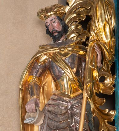 Zdjęcie nr 1: Całopostaciowa, ścięta z tyłu figura św. Floriana stojącego na niewysokiej podstawie i zwróconego w trzech czwartych w prawo. Sylwetka świętego jest w C-kształtnym układzie. Pochyloną  lekko głowę charakteryzuje pociągła twarz o wyrazistych rysach, półprzymkniętych oczach, długim nosie, zaróżowionych policzkach, nieznacznie rozchylonych ustach i krótkim, ciemnym zaroście. Ciemnobrązowe włosy skręcone w pukle rytmicznie opadają na kark. Święty jest ubrany w srebrzono-złoconą zbroję, przez prawe ramię przewiązana diagonalnie złocona wstęga, spięty na piersiach, złocony płaszcz opada na plecy i ramiona. Na głowie złocona mitra. W prawej, opuszczonej w dół ręce trzyma przechylony cebrzyk z wodą, lewą podtrzymuje złocony sztandar. Przy prawej nodze ma płonący budynek z bramą, krenelażem i oknem.   