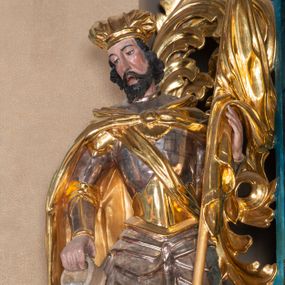 Zdjęcie nr 1: Całopostaciowa, ścięta z tyłu figura św. Floriana stojącego na niewysokiej podstawie i zwróconego w trzech czwartych w prawo. Sylwetka świętego jest w C-kształtnym układzie. Pochyloną  lekko głowę charakteryzuje pociągła twarz o wyrazistych rysach, półprzymkniętych oczach, długim nosie, zaróżowionych policzkach, nieznacznie rozchylonych ustach i krótkim, ciemnym zaroście. Ciemnobrązowe włosy skręcone w pukle rytmicznie opadają na kark. Święty jest ubrany w srebrzono-złoconą zbroję, przez prawe ramię przewiązana diagonalnie złocona wstęga, spięty na piersiach, złocony płaszcz opada na plecy i ramiona. Na głowie złocona mitra. W prawej, opuszczonej w dół ręce trzyma przechylony cebrzyk z wodą, lewą podtrzymuje złocony sztandar. Przy prawej nodze ma płonący budynek z bramą, krenelażem i oknem.   