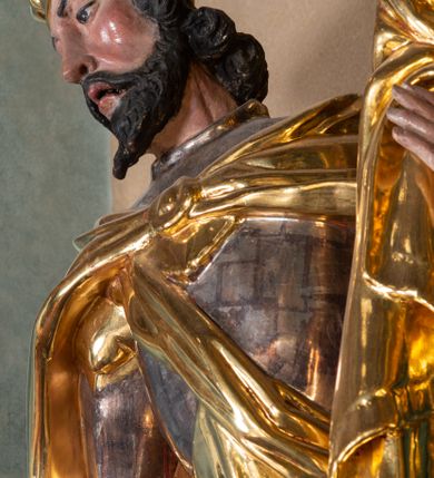 Zdjęcie nr 4: Całopostaciowa, ścięta z tyłu figura św. Wacława stojącego na sferycznej podstawie i zwróconego na wprost. Sylwetka świętego jest w S-kształtnym układzie. Pociągłą twarz charakteryzują wyraziste rysy o małych oczach, długim nosie, zaróżowionych policzkach i krótkim, ciemnym zaroście. Ciemnobrązowe włosy skręcone w pukle rytmicznie opadające sięgając ramion. Święty ubrany jest w srebrzoną zbroję, przez prawe ramię przewiązana diagonalnie złota wstęga, spięty na piersiach, złocony płaszcz opada na plecy i ramiona. Na głowie złocona mitra książęca. W prawej, zgiętej w łokciu i uniesionej do góry ręce trzyma złocone berło, w lewej, opuszczonej wzdłuż ciała złocony miecz.    