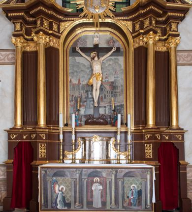 Zdjęcie nr 1: Ołtarz architektoniczny, jednokondygnacyjny, jednoosiowy ze zwieńczeniem i z parą bramek. Ołtarz murowany, prostopadłościenny z malowanym na płótnie antepedium ujętym drewnianą, profilowaną ramą. Wewnątrz przedstawienie wkomponowane w trójprzelotową arkadę z wizerunkiem Jezusa pośrodku i sceną Zwiastowania po bokach. Osadzone na niewysokim cokole tabernakulum jest w formie prostopadłościennej szafki o wypukłej ściance frontowej i narożach artykułowanych skośnie ustawionymi pilastrami wspierającymi wyłamujący się ponad nimi gzyms wieńczący przybierający po środku formę stykających się wolut z motywem konchy. Kwadratowe drzwiczki zamknięte są półkolistym łukiem nadwieszonym. Tabernakulum flankuje para wydatnych spływów wolutowych o krawędziach zdobionych motywem rocaille’owego grzebienia. Struktura jest srebrzona i złocona. Retabulum osadzone na zdwojonym, ukośnie zryzalitowanym cokole z otworami bramek na bokach. Część środkową nastawy ujmują dwie pary kolumn o kapitelach korynckich ustawione na tle pary filarów o kanelowanych trzonach, całość wspiera wyłamujące się ponad nimi przerwane w partii architrawu i fryzu belkowanie z silnie wysuniętym gzymsem. Zwieńczenie w formie przerwanego  przyczółka w kształcie S-kształtnych wolut. Górną partię cokołu zdobią motywy rocaille’ów, natomiast fryz motywy rozet. Pośrodku zwieńczenia usytuowana jest okrągła, promienista gloria z monogramem imienia Jezus i gorejącym sercem pośrodku. Po bokach zwieńczenia stoi para figur aniołów ubranych w niebieskie szaty. Pole środkowe retabulum w formie wnęki w kształcie stojącego prostokąta zamkniętego łukiem koszowym. Wewnątrz krucyfiks na polichromowanym tle przestawiającym widok miasta z murami warownymi i wydatną bryłą kościoła po prawej stronie kompozycji, pokrytym skłębionymi chmurami niebem oraz tarczami - słoneczną po prawej i księżycową po lewej stronie górnej partii krucyfiksu. Struktura ołtarza  jest w kolorze brązowym, detal architektoniczny i ornamentyka są złocone i srebrzone.      