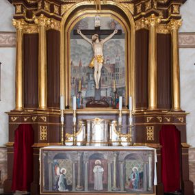 Zdjęcie nr 1: Ołtarz architektoniczny, jednokondygnacyjny, jednoosiowy ze zwieńczeniem i z parą bramek. Ołtarz murowany, prostopadłościenny z malowanym na płótnie antepedium ujętym drewnianą, profilowaną ramą. Wewnątrz przedstawienie wkomponowane w trójprzelotową arkadę z wizerunkiem Jezusa pośrodku i sceną Zwiastowania po bokach. Osadzone na niewysokim cokole tabernakulum jest w formie prostopadłościennej szafki o wypukłej ściance frontowej i narożach artykułowanych skośnie ustawionymi pilastrami wspierającymi wyłamujący się ponad nimi gzyms wieńczący przybierający po środku formę stykających się wolut z motywem konchy. Kwadratowe drzwiczki zamknięte są półkolistym łukiem nadwieszonym. Tabernakulum flankuje para wydatnych spływów wolutowych o krawędziach zdobionych motywem rocaille’owego grzebienia. Struktura jest srebrzona i złocona. Retabulum osadzone na zdwojonym, ukośnie zryzalitowanym cokole z otworami bramek na bokach. Część środkową nastawy ujmują dwie pary kolumn o kapitelach korynckich ustawione na tle pary filarów o kanelowanych trzonach, całość wspiera wyłamujące się ponad nimi przerwane w partii architrawu i fryzu belkowanie z silnie wysuniętym gzymsem. Zwieńczenie w formie przerwanego  przyczółka w kształcie S-kształtnych wolut. Górną partię cokołu zdobią motywy rocaille’ów, natomiast fryz motywy rozet. Pośrodku zwieńczenia usytuowana jest okrągła, promienista gloria z monogramem imienia Jezus i gorejącym sercem pośrodku. Po bokach zwieńczenia stoi para figur aniołów ubranych w niebieskie szaty. Pole środkowe retabulum w formie wnęki w kształcie stojącego prostokąta zamkniętego łukiem koszowym. Wewnątrz krucyfiks na polichromowanym tle przestawiającym widok miasta z murami warownymi i wydatną bryłą kościoła po prawej stronie kompozycji, pokrytym skłębionymi chmurami niebem oraz tarczami - słoneczną po prawej i księżycową po lewej stronie górnej partii krucyfiksu. Struktura ołtarza  jest w kolorze brązowym, detal architektoniczny i ornamentyka są złocone i srebrzone.      