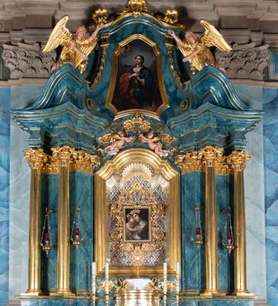 Zdjęcie nr 1: Ołtarz architektoniczny, jednokondygnacyjny, jednoosiowy ze zwieńczeniem. Ołtarz drewniany, prostopadłościenny, ustawiony na dwustopniowej podstawie. Antependium w formie leżącego prostokąta ujętego ramą dekorowaną akantem; w polu owalny medalion w wieńcu z monogramem maryjnym, wkomponowany w gęste wici suchego akantu.
Tabernakulum w formie drewnianej skrzynki na cokole o wklęsło-wypukłym licu, ujęte dwoma parami pilastrów o trzonach utworzonych z podwójnych spływów wolutowych; dźwigających pełne belkowanie opasujące ściankę frontową, wyłamane na osi podpór. Drzwiczki w formie stojącego prostokąta zamkniętego łukiem półkolistym nadwieszonym z krzyżem w polu, na którego przecięciu ramion medalion z monogramem imienia Jezus w glorii. Tron wystawienia w postaci podestu wspartego na pięciu kabłąkach. Struktura w całości srebrzona, podpory i profile złocone.
Nastawa osadzona na zdwojonym cokole, górny lekko wybrzuszony. Część środkowa ujęta parą pilastrów o kanelowanych trzonach i kapitelach kompozytowych zwróconych do wewnątrz lica ołtarza oraz trzema parami analogicznych pilastrów ustawionych pod kątem na zewnątrz przed którymi stoją dwie pary kolumn o kapitelach kompozytowych. Podpory dźwigają pełne belkowanie, przerwane belkowanie o lekko wybrzuszonym fryzie i wklęsłej linii gzymsu. Zwieńczenie ujęte parą spływów wolutowych i zamknięte fragmentem gzymsu w postaci łuku wklęsło-wypukłego. Całość flankuje przerwany, ustawiony skośnie, falisty przyczółek. Pole przerwanego belkowania wypełnia schweifwerk przechodzący w wić roślinną z motywami rozet oraz parą puttów podtrzymujących koronę. Spływy wolutowe zwieńczenia zdobią kampanule, oraz para wazonów, gzyms wieńczący zaś trzy konchy. Na przerwanym przyczółku para figur klęczących aniołów.  Pole części środkowej retabulum w formie głębokiej niszy w kształcie stojącego prostokąta zamkniętego łukiem odcinkowym łukiem nadwieszonym z uskokami, ujętej profilowaną ramą, we wnątrz znajduje się obraz Matki Boskiej Myślenickiej. W zwieńczeniu obraz w kształcie trapezu o wklęsłych ramionach, podstawie i narożach zamknięty łukiem wklęsło-wypukłym, ujęty profilowaną ramą, z wizerunkiem św. Tekli. 
Struktura w całości marmoryzowana w kolorze zielono-granatowym; kolumny, ornamentyka i profile złocone i srebrzone.

