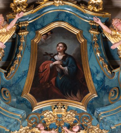 Zdjęcie nr 2:  Obraz w kształcie trapezu o wklęsłych ramionach, podstawie i narożach, nakrytego łukiem wklęsło-wypukłym, ujęty profilowaną, złoconą ramą przedstawia św. Teklę ukazaną w półpostaci, w trzech czwartych zwróconą w prawo. Uniesioną nieznacznie do góry głowę charkteryzuje owalna twarz o pełnych, subtelnych rysach młodej kobiety. Długie, brązowe, falowane włosy opadają na ramiona. Święta ubrana jest w białą spodnią suknię i niebieską wierzchnią z gorsetem. Wokół dekoltu zawiązana biała chusta, z ramion zsuwa się czerwony płaszcz. W złożonych na piersiach dłoniach trzyma krucyfiks. W lewym, dolnym rogu kompozycji jest brązowa sylwetka lwa, a w prawym dolnym wiązki płomieni. Wokół płaszcza świętej wiją się trzy czarne węże. Święta Tekla ukazana jest na tle szarych obłoków, spomiędzy których w lewym górnym rogu obrazu wynurza się para uskrzydlonych główek anielskich.  
Kolorystyka w ciemnej, niezbyt nasyconej tonacji.   