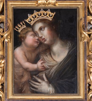 Zdjęcie nr 1: Obraz w kształcie stojącego prostokąta, ujęty profilowaną i ażurową, akantową, złoconą ramą, z przedstawieniem Matki Boskiej z Dzieciątkiem. Maria ukazana w półpostaci, w trzech czwartych zwrócona i lekko pochylona w prawo. Głowa w trzech czwartych przechylona w prawo. Twarz owalna o delikatnych, pełnych rysach. Włosy długie, ciemnobrązowe. Maria ubrana w białą tunikę i otulona ciemnoniebieskim płaszczem. Lewą ręką, podniesiona na wysokości klatki piersiowej, wskazuje na stojące po jej prawej stronie Dzieciątko. Jezus w trzech czwartych zwrócony w lewo, głowę o zaokrąglonej twarzy i z krótkimi, blond, kręconymi włosami, przytula do twarzy Marii. Lewą rączką obejmuje szyję Marii, prawą trzyma połę jej płaszcza. Ciało Dzieciątka od pasa przesłonięte delikatną, przejrzystą tkaniną. Tło ciemne. Na głowach postaci nakładane złocone korony. 
Kolorystyka wysublimowana, stonowana, niezbyt nasyconej tonacji.   
