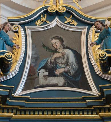 Zdjęcie nr 2: Ołtarz architektoniczny, jednokondygnacyjny, jednoosiowy, ze zwieńczeniem. Ołtarz drewniany, sarkofagowy, z dostawionym prostokątnym, drewnianym antepedium. Pole antepedium zdobione dekoracją polichromowaną na błękitnym tle, z formą kartusza z monogramem maryjnym pośrodku, ujętym ornamentyką akantową oraz parą aniołków. Retabulum na zdwojonym cokole o zryzalitowanych, lekko ukośnie ustawionych bokach, ujęte dwoma parami pilastrów i parą kolumn korynckich o żłobkowanych trzonach, wspierających wyłamujące się ponad nimi, przerwane w partii architrawu i fryzu belkowanie z silnie wysuniętym gzymsem. Zwieńczenie w formie stojącego prostokąta ujętego po bokach parą spływów wolutowych, zamknięte parą przeciwstawnie ustawionych, stykających się wolut. Szczyt w formie okrągłej, ażurowej, promienistej glorii z monogramem maryjnym. Zwieńczenie flankowane przerwanym wolutowym przyczółkiem oraz parą wazonów. Pola boczne cokołu retabulum zdobione motywem wydłużonych rozet. W polu środkowym trójdzielna płycina w kształcie leżącego prostokąta, z wizerunkiem Matki Boskiej Ostrobramskiej oraz napisem „MATKO MIŁO/SIERDZIA / PRZYJMIJ / NASZE / CIERPIENIA / 1994 / + BŁOGO/SŁAWIENI / MIŁO/SIERNI”.  Retabulum ujęte parą ażurowych, akantowych uszaków z wplecionym motywem liści laurowych. W dolnej partii środkowej części retabulum płycina o fantazyjnym wykroju z inskrypcją „Fondatorowie Ułtarza / Woyciech y Agniszka z Łopatów Mrowczeńscy / dnia 5go Listopada 1827”.  W górnej części zamknięta korona z podwieszoną parą wolut w formie stylizowanej wici roślinnej. W dolnej partii wnęki retabulum wazon z wolutowo kształtującymi się wiciami akantowymi, u góry motyw lambrekinu. Części fryzu retabulum zdobione rozetami. W partii gzymsu ornament kostkowy. Spływy wolutowe zwieńczenia zdobione grzebieniem rocaille'owym oraz gałązką laurową. W górnej partii zwieńczenia motyw dwóch gałązek różanych. Całość flankowana parą wazonów z kwiatem lilii. Pole środkowe w formie wnęki w kształcie stojącego prostokąta zamkniętego łukiem wycinkowym uskokowym, nadwieszonym, ujęte profilowaną złoconą i srebrzoną ramą. Wewnątrz obraz Matki Boskiej Szkaplerznej.  W zwieńczeniu pole w kształcie trapezu o wklęsłych ramionach i podstawie, zamkniętego łukiem kotarowym, ujęte profilowaną, srebrzoną ramą. Wewnątrz obraz św. Agnieszki. Na przerwanym przyczółku para klęczących aniołków. 
Struktura polichromowana w odcieniu ciemnego turkusu. Detal architektoniczny i ornamentyka złocone oraz srebrzone. 