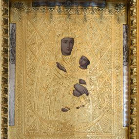 Zdjęcie nr 1: Obraz w kształcie stojącego prostokąta z przedstawieniem Matki Boskiej z Dzieciątkiem ukazanej w półpostaci, nieznacznie zwróconej w lewo. Owalną twarz charakteryzują wyraziste, delikatnie modelowane rysy o dużych oczach, długim nosie i wydatnych ustach. Rękami o skrzyżowanych dłoniach, z wyprostowanymi palcami prawej ręki, podtrzymuje siedzące na jej lewym ramieniu Dzieciątko. Jezus zwrócony jest w trzech czwartych w prawo. Lekko odchyloną głowę charakteryzuje owalna twarz o  wyrazistych, delikatnie modelowanych rysach o dużych oczach, długim nosie i wydatnych ustach. Dzieciątko prawą rękę wyciąga przed siebie w geście błogosławieństwa, lewą podtrzymuje zamkniętą księgę. Obraz pokryty jest metalową blachą, w której zaznaczony jest zarys ubioru postaci. Maria ma na sobie suknię i osłaniający szczelnie sylwetkę, nałożony na głowę płaszcz. Jezus ubrany jest w długą suknię. Szaty zdobi ornamentyka roślinna z motywami gwiazd. Głowy postaci w koronach zamkniętych okalają nimby z promienistą glorią w środku. Tło obrazu pokrywa motyw romboidalnej kraty z motywami rozet.  U dołu postaci wąski sierp księżyca. Przedstawienie ujęte pasami ornamentu cekinowego z rozetami w narożach.      
