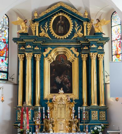 Zdjęcie nr 1: Ołtarz przyścienny, jednokondygnacyjny, jednoosiowy, ze zwieńczeniem. Ołtarz prostopadłościenny, tabernakulum z tronem wystawienia w formie architektonicznej na rzucie trapezoidalnym. W przedniej ściance wysokiego cokołu, o narożach ujętych spływami wolutowymi, są drzwiczki w kształcie prostokąta zamkniętego półkolistym łukiem nadwieszonym zdobione płaskorzeźbionym przedstawieniem kielicha eucharystycznego. Cokół wieńczy gzyms przekształcający się pośrodku w parę stykających się wolut. Na występach nad spływami cokołu osadzone kolumienki wspierające wyłamujące się ponad nimi belkowanie baldachimu tronu wystawienia. Zwieńczenie w formie pary stykających się spływów wolutowych z motywem paludamentu. Zaplecek zdobiony płycinami z ornamentalnymi obramieniami z motywami rocaille’u, w górnej partii płaskorzeźbiony trójkąt z okiem Opatrzności Bożej ujęty promienistą glorią. W zwieńczeniu para wazonów i para figurek aniołków, na szczycie księga z siedmioma pieczęciami i leżącym barankiem paschalnym.  
Retabulum osadzone na zdwojonym cokole, w górnej partii o zryzalitowanych bokach. Część środkową ujmują trzy pary kolumn, z których środkowe wysunięte, wspierających przerwane w partii architrawu i fryzu belkowanie. Zwieńczenie ujęte parą kolumn wspierających gzyms w formie trójkątnego przyczółka. Pola cokołu retabulum wypełnia stylizowana ornamentyka roślinna, partie fryzu oraz górne naroża części środkowej zdobią uskrzydlone główki anielskie, a gzyms kostkowanie. Zwieńczenie ujęte po bokach motywem liści paproci, pole ulistnionymi gałązkami z wstążką. Krawędź gzymsu wieńczącego zdobi wić roślinna z krzyżem pośrodku, po bokach para wazonów. Całość ujmuje para figur klęczących aniołów. Pole części środkowej w kształcie stojącego prostokąta ujętego profilowaną, złoconą ramą z przedstawieniem Narodzenia Najświętszej Marii Panny. W zwieńczeniu obraz w kształcie stojącego owalu, ujętego ramą zdobioną akantowymi liśćmi, z wizerunkiem św. Mikołaja. Struktura marmoryzowana w odcieniach błękitów, detal architektoniczny i ornamentyka złocone.   
