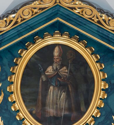 Zdjęcie nr 13: Ołtarz przyścienny, jednokondygnacyjny, jednoosiowy, ze zwieńczeniem. Ołtarz prostopadłościenny, tabernakulum z tronem wystawienia w formie architektonicznej na rzucie trapezoidalnym. W przedniej ściance wysokiego cokołu, o narożach ujętych spływami wolutowymi, są drzwiczki w kształcie prostokąta zamkniętego półkolistym łukiem nadwieszonym zdobione płaskorzeźbionym przedstawieniem kielicha eucharystycznego. Cokół wieńczy gzyms przekształcający się pośrodku w parę stykających się wolut. Na występach nad spływami cokołu osadzone kolumienki wspierające wyłamujące się ponad nimi belkowanie baldachimu tronu wystawienia. Zwieńczenie w formie pary stykających się spływów wolutowych z motywem paludamentu. Zaplecek zdobiony płycinami z ornamentalnymi obramieniami z motywami rocaille’u, w górnej partii płaskorzeźbiony trójkąt z okiem Opatrzności Bożej ujęty promienistą glorią. W zwieńczeniu para wazonów i para figurek aniołków, na szczycie księga z siedmioma pieczęciami i leżącym barankiem paschalnym.  
Retabulum osadzone na zdwojonym cokole, w górnej partii o zryzalitowanych bokach. Część środkową ujmują trzy pary kolumn, z których środkowe wysunięte, wspierających przerwane w partii architrawu i fryzu belkowanie. Zwieńczenie ujęte parą kolumn wspierających gzyms w formie trójkątnego przyczółka. Pola cokołu retabulum wypełnia stylizowana ornamentyka roślinna, partie fryzu oraz górne naroża części środkowej zdobią uskrzydlone główki anielskie, a gzyms kostkowanie. Zwieńczenie ujęte po bokach motywem liści paproci, pole ulistnionymi gałązkami z wstążką. Krawędź gzymsu wieńczącego zdobi wić roślinna z krzyżem pośrodku, po bokach para wazonów. Całość ujmuje para figur klęczących aniołów. Pole części środkowej w kształcie stojącego prostokąta ujętego profilowaną, złoconą ramą z przedstawieniem Narodzenia Najświętszej Marii Panny. W zwieńczeniu obraz w kształcie stojącego owalu, ujętego ramą zdobioną akantowymi liśćmi, z wizerunkiem św. Mikołaja. Struktura marmoryzowana w odcieniach błękitów, detal architektoniczny i ornamentyka złocone.   
