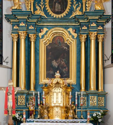 Zdjęcie nr 3: Ołtarz przyścienny, jednokondygnacyjny, jednoosiowy, ze zwieńczeniem. Ołtarz prostopadłościenny, tabernakulum z tronem wystawienia w formie architektonicznej na rzucie trapezoidalnym. W przedniej ściance wysokiego cokołu, o narożach ujętych spływami wolutowymi, są drzwiczki w kształcie prostokąta zamkniętego półkolistym łukiem nadwieszonym zdobione płaskorzeźbionym przedstawieniem kielicha eucharystycznego. Cokół wieńczy gzyms przekształcający się pośrodku w parę stykających się wolut. Na występach nad spływami cokołu osadzone kolumienki wspierające wyłamujące się ponad nimi belkowanie baldachimu tronu wystawienia. Zwieńczenie w formie pary stykających się spływów wolutowych z motywem paludamentu. Zaplecek zdobiony płycinami z ornamentalnymi obramieniami z motywami rocaille’u, w górnej partii płaskorzeźbiony trójkąt z okiem Opatrzności Bożej ujęty promienistą glorią. W zwieńczeniu para wazonów i para figurek aniołków, na szczycie księga z siedmioma pieczęciami i leżącym barankiem paschalnym.  
Retabulum osadzone na zdwojonym cokole, w górnej partii o zryzalitowanych bokach. Część środkową ujmują trzy pary kolumn, z których środkowe wysunięte, wspierających przerwane w partii architrawu i fryzu belkowanie. Zwieńczenie ujęte parą kolumn wspierających gzyms w formie trójkątnego przyczółka. Pola cokołu retabulum wypełnia stylizowana ornamentyka roślinna, partie fryzu oraz górne naroża części środkowej zdobią uskrzydlone główki anielskie, a gzyms kostkowanie. Zwieńczenie ujęte po bokach motywem liści paproci, pole ulistnionymi gałązkami z wstążką. Krawędź gzymsu wieńczącego zdobi wić roślinna z krzyżem pośrodku, po bokach para wazonów. Całość ujmuje para figur klęczących aniołów. Pole części środkowej w kształcie stojącego prostokąta ujętego profilowaną, złoconą ramą z przedstawieniem Narodzenia Najświętszej Marii Panny. W zwieńczeniu obraz w kształcie stojącego owalu, ujętego ramą zdobioną akantowymi liśćmi, z wizerunkiem św. Mikołaja. Struktura marmoryzowana w odcieniach błękitów, detal architektoniczny i ornamentyka złocone.   
