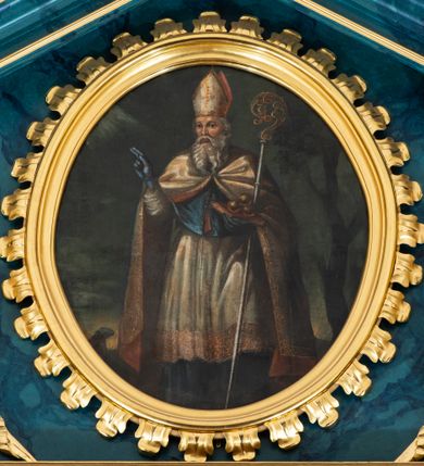 Zdjęcie nr 14: Ołtarz przyścienny, jednokondygnacyjny, jednoosiowy, ze zwieńczeniem. Ołtarz prostopadłościenny, tabernakulum z tronem wystawienia w formie architektonicznej na rzucie trapezoidalnym. W przedniej ściance wysokiego cokołu, o narożach ujętych spływami wolutowymi, są drzwiczki w kształcie prostokąta zamkniętego półkolistym łukiem nadwieszonym zdobione płaskorzeźbionym przedstawieniem kielicha eucharystycznego. Cokół wieńczy gzyms przekształcający się pośrodku w parę stykających się wolut. Na występach nad spływami cokołu osadzone kolumienki wspierające wyłamujące się ponad nimi belkowanie baldachimu tronu wystawienia. Zwieńczenie w formie pary stykających się spływów wolutowych z motywem paludamentu. Zaplecek zdobiony płycinami z ornamentalnymi obramieniami z motywami rocaille’u, w górnej partii płaskorzeźbiony trójkąt z okiem Opatrzności Bożej ujęty promienistą glorią. W zwieńczeniu para wazonów i para figurek aniołków, na szczycie księga z siedmioma pieczęciami i leżącym barankiem paschalnym.  
Retabulum osadzone na zdwojonym cokole, w górnej partii o zryzalitowanych bokach. Część środkową ujmują trzy pary kolumn, z których środkowe wysunięte, wspierających przerwane w partii architrawu i fryzu belkowanie. Zwieńczenie ujęte parą kolumn wspierających gzyms w formie trójkątnego przyczółka. Pola cokołu retabulum wypełnia stylizowana ornamentyka roślinna, partie fryzu oraz górne naroża części środkowej zdobią uskrzydlone główki anielskie, a gzyms kostkowanie. Zwieńczenie ujęte po bokach motywem liści paproci, pole ulistnionymi gałązkami z wstążką. Krawędź gzymsu wieńczącego zdobi wić roślinna z krzyżem pośrodku, po bokach para wazonów. Całość ujmuje para figur klęczących aniołów. Pole części środkowej w kształcie stojącego prostokąta ujętego profilowaną, złoconą ramą z przedstawieniem Narodzenia Najświętszej Marii Panny. W zwieńczeniu obraz w kształcie stojącego owalu, ujętego ramą zdobioną akantowymi liśćmi, z wizerunkiem św. Mikołaja. Struktura marmoryzowana w odcieniach błękitów, detal architektoniczny i ornamentyka złocone.   
