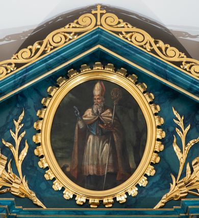 Zdjęcie nr 12: Ołtarz przyścienny, jednokondygnacyjny, jednoosiowy, ze zwieńczeniem. Ołtarz prostopadłościenny, tabernakulum z tronem wystawienia w formie architektonicznej na rzucie trapezoidalnym. W przedniej ściance wysokiego cokołu, o narożach ujętych spływami wolutowymi, są drzwiczki w kształcie prostokąta zamkniętego półkolistym łukiem nadwieszonym zdobione płaskorzeźbionym przedstawieniem kielicha eucharystycznego. Cokół wieńczy gzyms przekształcający się pośrodku w parę stykających się wolut. Na występach nad spływami cokołu osadzone kolumienki wspierające wyłamujące się ponad nimi belkowanie baldachimu tronu wystawienia. Zwieńczenie w formie pary stykających się spływów wolutowych z motywem paludamentu. Zaplecek zdobiony płycinami z ornamentalnymi obramieniami z motywami rocaille’u, w górnej partii płaskorzeźbiony trójkąt z okiem Opatrzności Bożej ujęty promienistą glorią. W zwieńczeniu para wazonów i para figurek aniołków, na szczycie księga z siedmioma pieczęciami i leżącym barankiem paschalnym.  
Retabulum osadzone na zdwojonym cokole, w górnej partii o zryzalitowanych bokach. Część środkową ujmują trzy pary kolumn, z których środkowe wysunięte, wspierających przerwane w partii architrawu i fryzu belkowanie. Zwieńczenie ujęte parą kolumn wspierających gzyms w formie trójkątnego przyczółka. Pola cokołu retabulum wypełnia stylizowana ornamentyka roślinna, partie fryzu oraz górne naroża części środkowej zdobią uskrzydlone główki anielskie, a gzyms kostkowanie. Zwieńczenie ujęte po bokach motywem liści paproci, pole ulistnionymi gałązkami z wstążką. Krawędź gzymsu wieńczącego zdobi wić roślinna z krzyżem pośrodku, po bokach para wazonów. Całość ujmuje para figur klęczących aniołów. Pole części środkowej w kształcie stojącego prostokąta ujętego profilowaną, złoconą ramą z przedstawieniem Narodzenia Najświętszej Marii Panny. W zwieńczeniu obraz w kształcie stojącego owalu, ujętego ramą zdobioną akantowymi liśćmi, z wizerunkiem św. Mikołaja. Struktura marmoryzowana w odcieniach błękitów, detal architektoniczny i ornamentyka złocone.   
