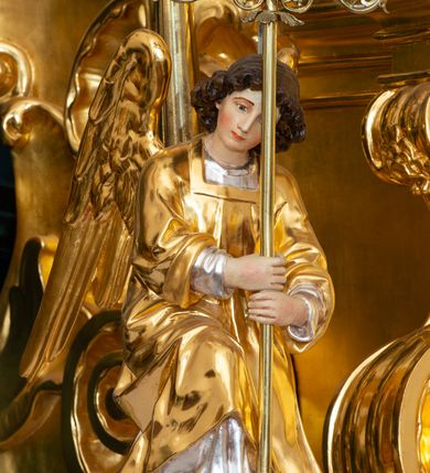 Zdjęcie nr 20: Ołtarz przyścienny, jednokondygnacyjny, jednoosiowy, ze zwieńczeniem. Ołtarz prostopadłościenny, tabernakulum z tronem wystawienia w formie architektonicznej na rzucie trapezoidalnym. W przedniej ściance wysokiego cokołu, o narożach ujętych spływami wolutowymi, są drzwiczki w kształcie prostokąta zamkniętego półkolistym łukiem nadwieszonym zdobione płaskorzeźbionym przedstawieniem kielicha eucharystycznego. Cokół wieńczy gzyms przekształcający się pośrodku w parę stykających się wolut. Na występach nad spływami cokołu osadzone kolumienki wspierające wyłamujące się ponad nimi belkowanie baldachimu tronu wystawienia. Zwieńczenie w formie pary stykających się spływów wolutowych z motywem paludamentu. Zaplecek zdobiony płycinami z ornamentalnymi obramieniami z motywami rocaille’u, w górnej partii płaskorzeźbiony trójkąt z okiem Opatrzności Bożej ujęty promienistą glorią. W zwieńczeniu para wazonów i para figurek aniołków, na szczycie księga z siedmioma pieczęciami i leżącym barankiem paschalnym.  
Retabulum osadzone na zdwojonym cokole, w górnej partii o zryzalitowanych bokach. Część środkową ujmują trzy pary kolumn, z których środkowe wysunięte, wspierających przerwane w partii architrawu i fryzu belkowanie. Zwieńczenie ujęte parą kolumn wspierających gzyms w formie trójkątnego przyczółka. Pola cokołu retabulum wypełnia stylizowana ornamentyka roślinna, partie fryzu oraz górne naroża części środkowej zdobią uskrzydlone główki anielskie, a gzyms kostkowanie. Zwieńczenie ujęte po bokach motywem liści paproci, pole ulistnionymi gałązkami z wstążką. Krawędź gzymsu wieńczącego zdobi wić roślinna z krzyżem pośrodku, po bokach para wazonów. Całość ujmuje para figur klęczących aniołów. Pole części środkowej w kształcie stojącego prostokąta ujętego profilowaną, złoconą ramą z przedstawieniem Narodzenia Najświętszej Marii Panny. W zwieńczeniu obraz w kształcie stojącego owalu, ujętego ramą zdobioną akantowymi liśćmi, z wizerunkiem św. Mikołaja. Struktura marmoryzowana w odcieniach błękitów, detal architektoniczny i ornamentyka złocone.   
